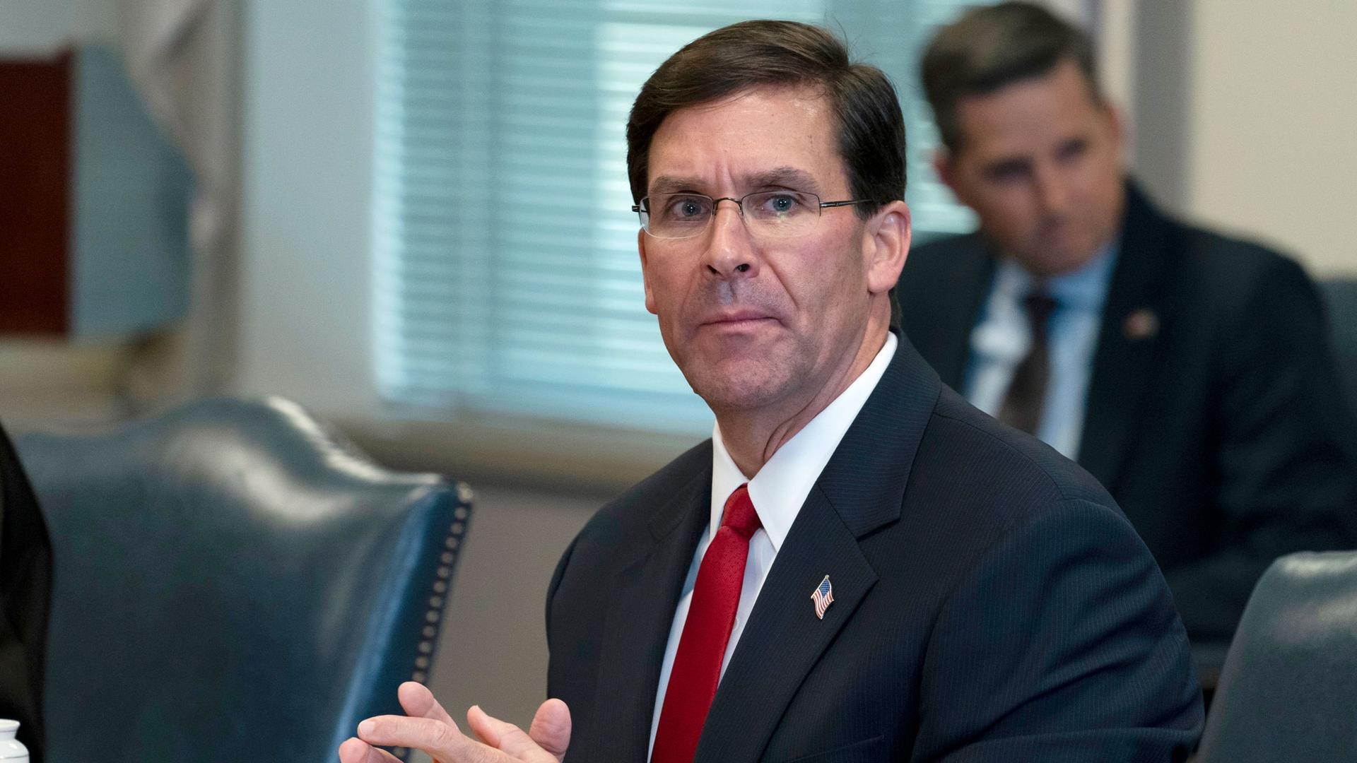 Secretary of Defense Mark Esper is shown seated a table with his hands clasped.