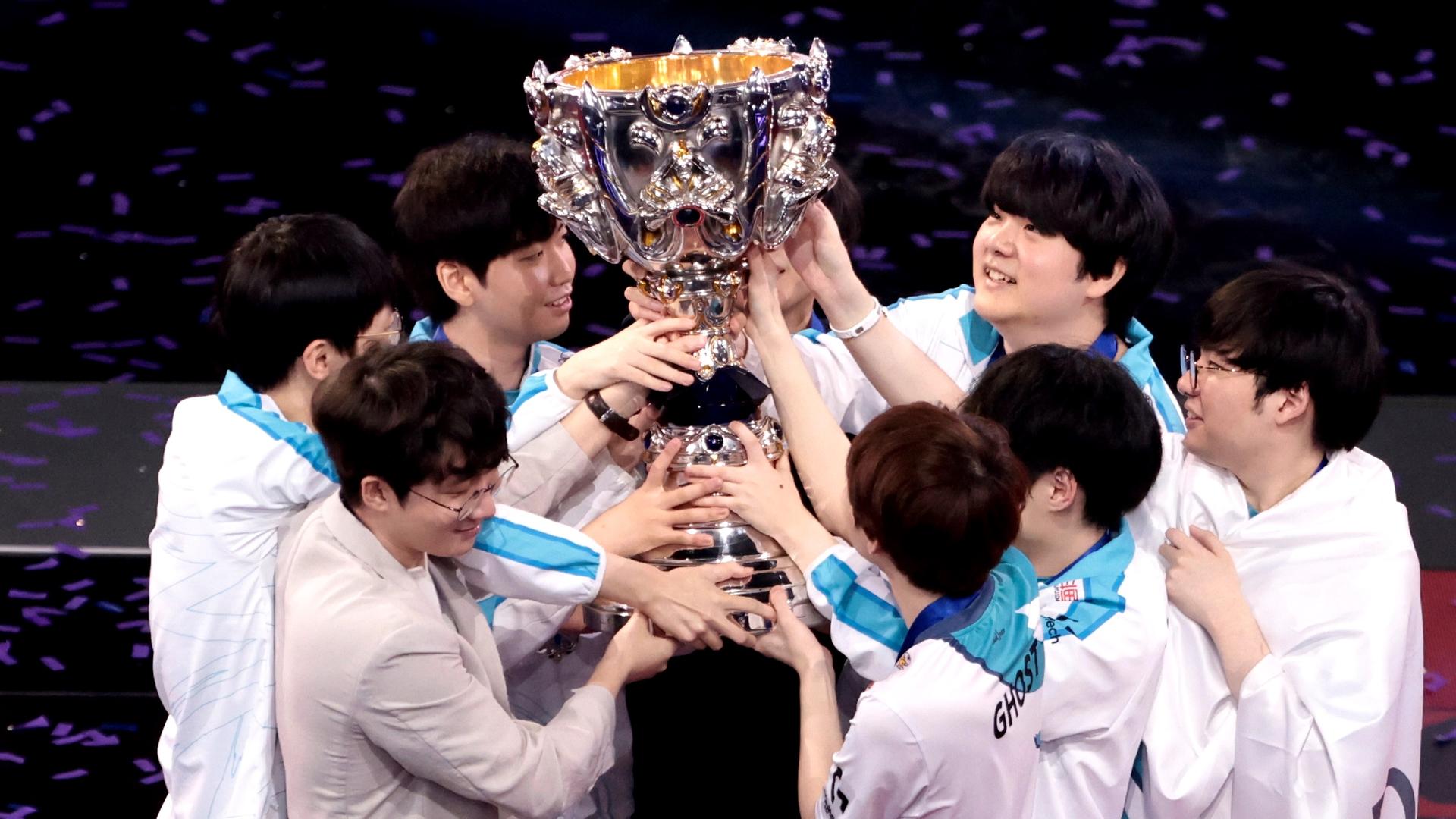 A group of Korean young men huddle around and hold up a trophy. 