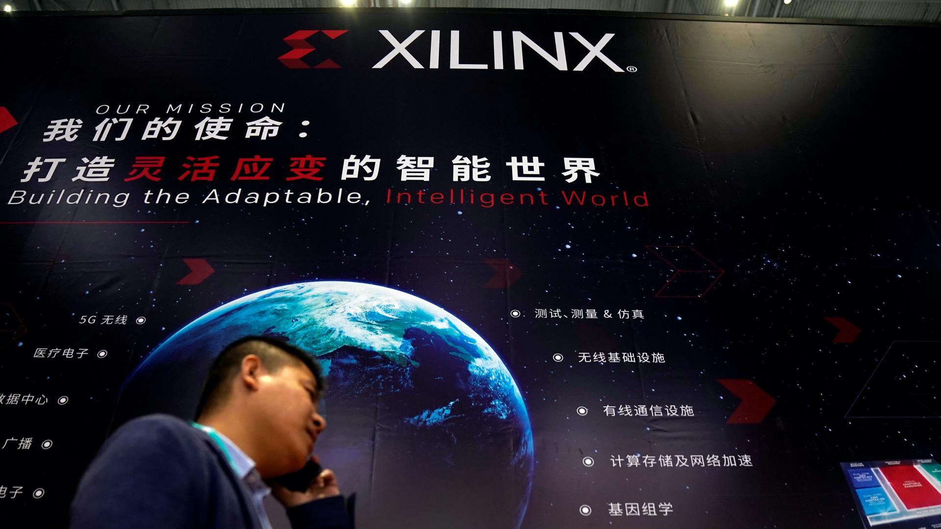 A man stands in front of a large company sign with an image of a globe on it and Mandarin text written next to it. 