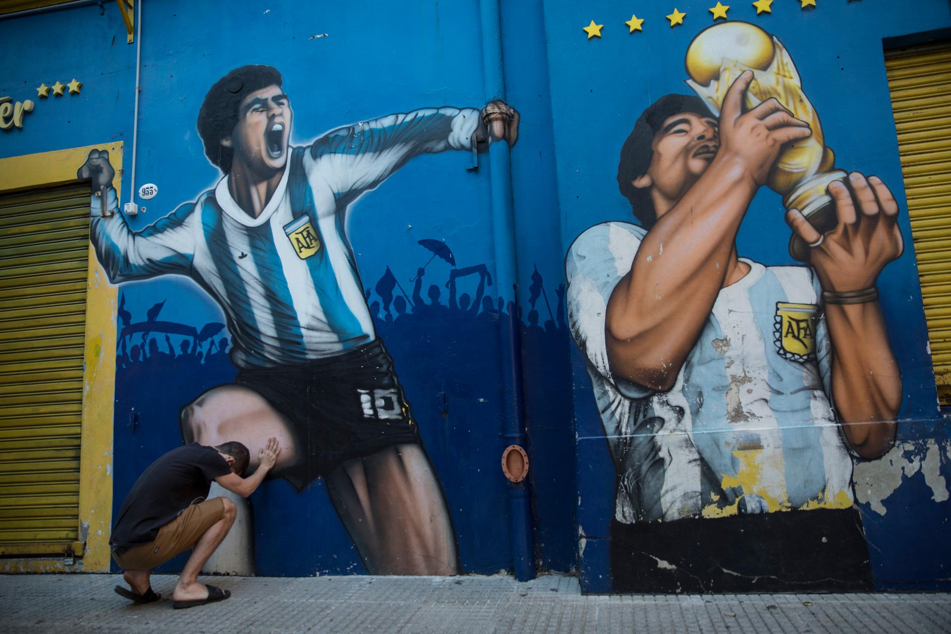 A man prays while touching a painting of Diego Maradona near the Boca Juniors stadium in Buenos Aires, Argentina, Nov. 27, 2020.