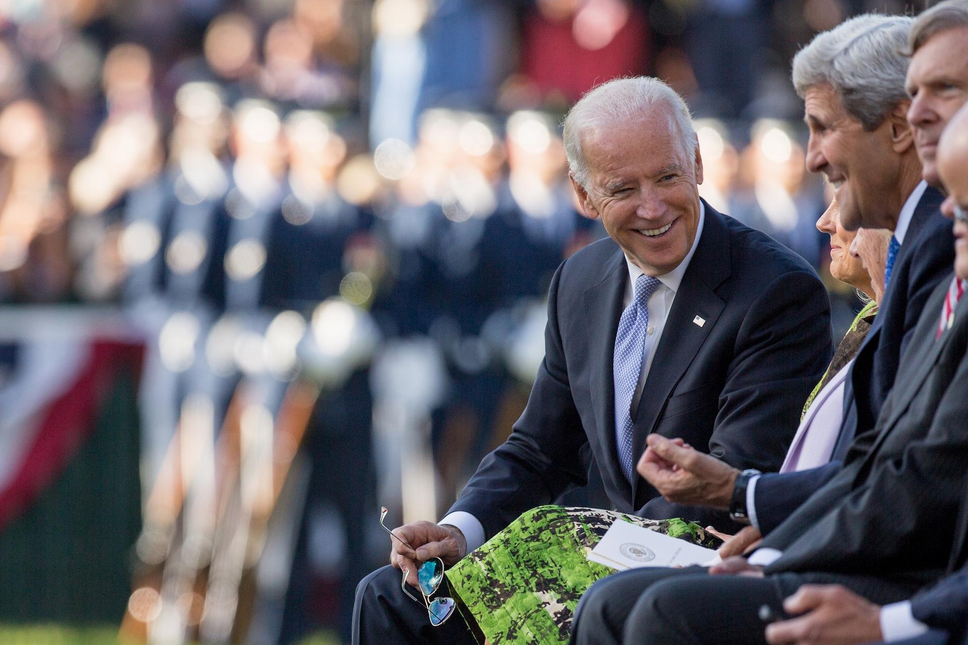 Joe Biden sitting next to John Kerry at an event in 2015