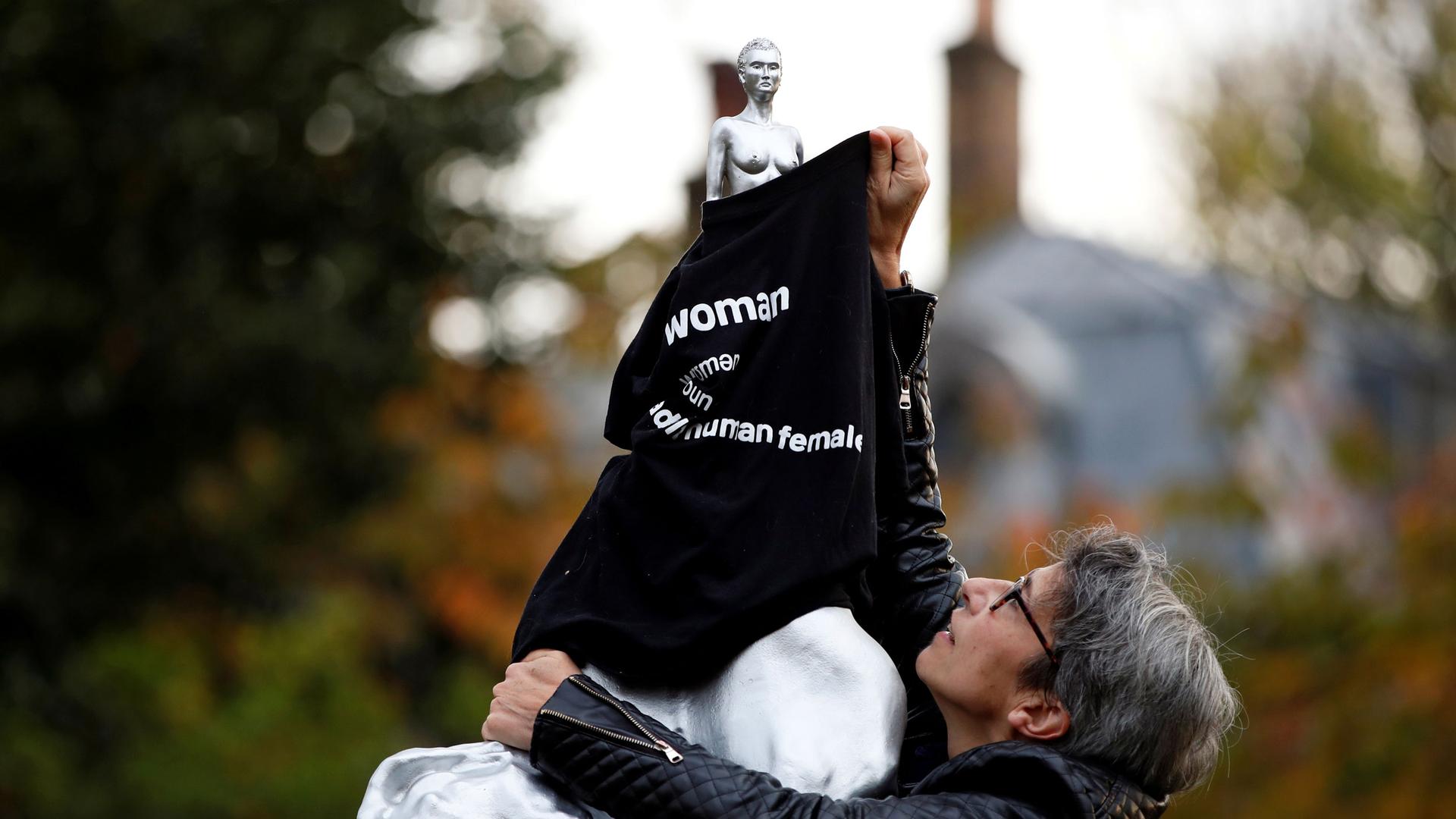 A woman is shown covering a nude silver statue with a black T-shirt with the word, 