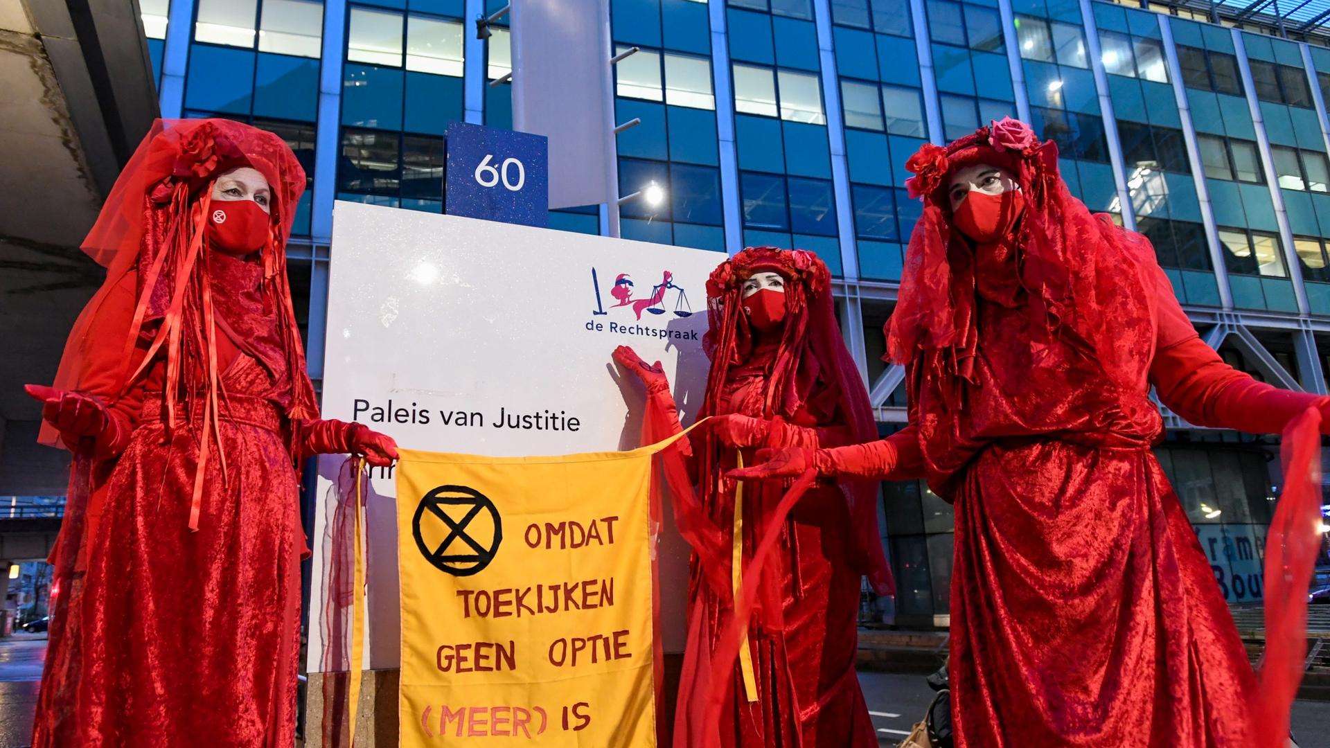 Environmental activists hold a banner that reads: "Because watching is not an option [anymore]," as they protest outside of a court during a hearing in a case environmentalist and human rights groups have brought against Royal Dutch Shell to force the ene