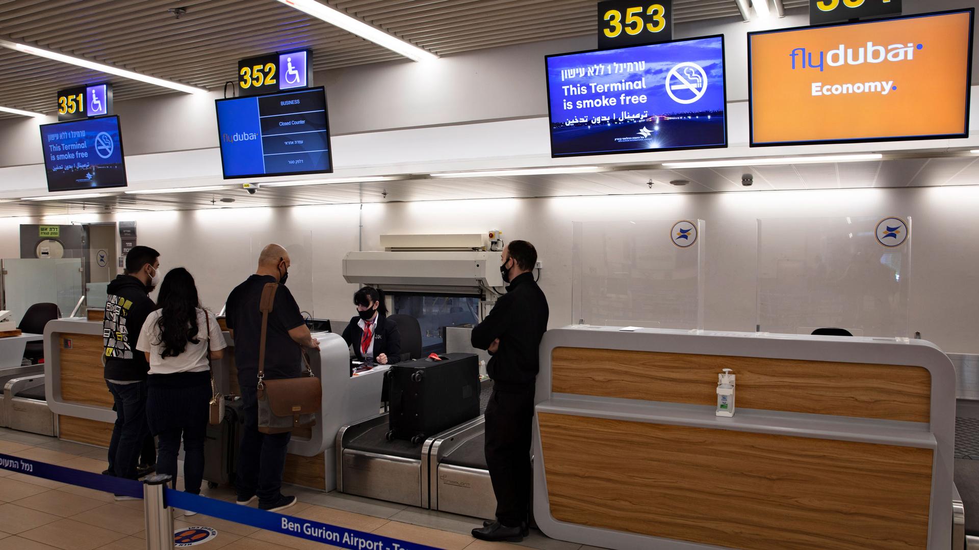 A group of three people are shown from behind standing at a ticketing agent desk at Ben Gurion airport.