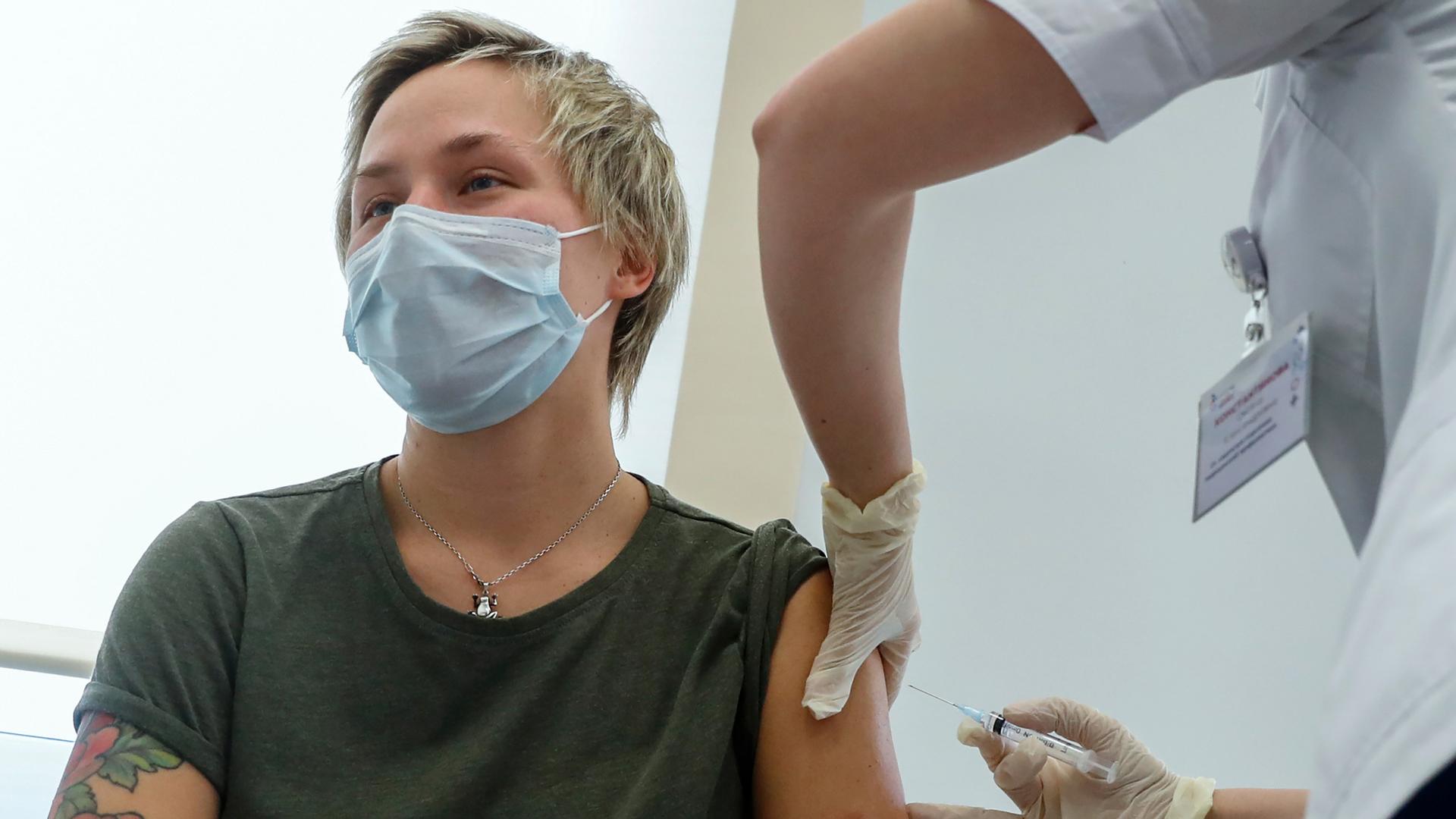 A person is shown with their shirt sleeve rolled up and receiving an injection in their shoulder by a medical professional.