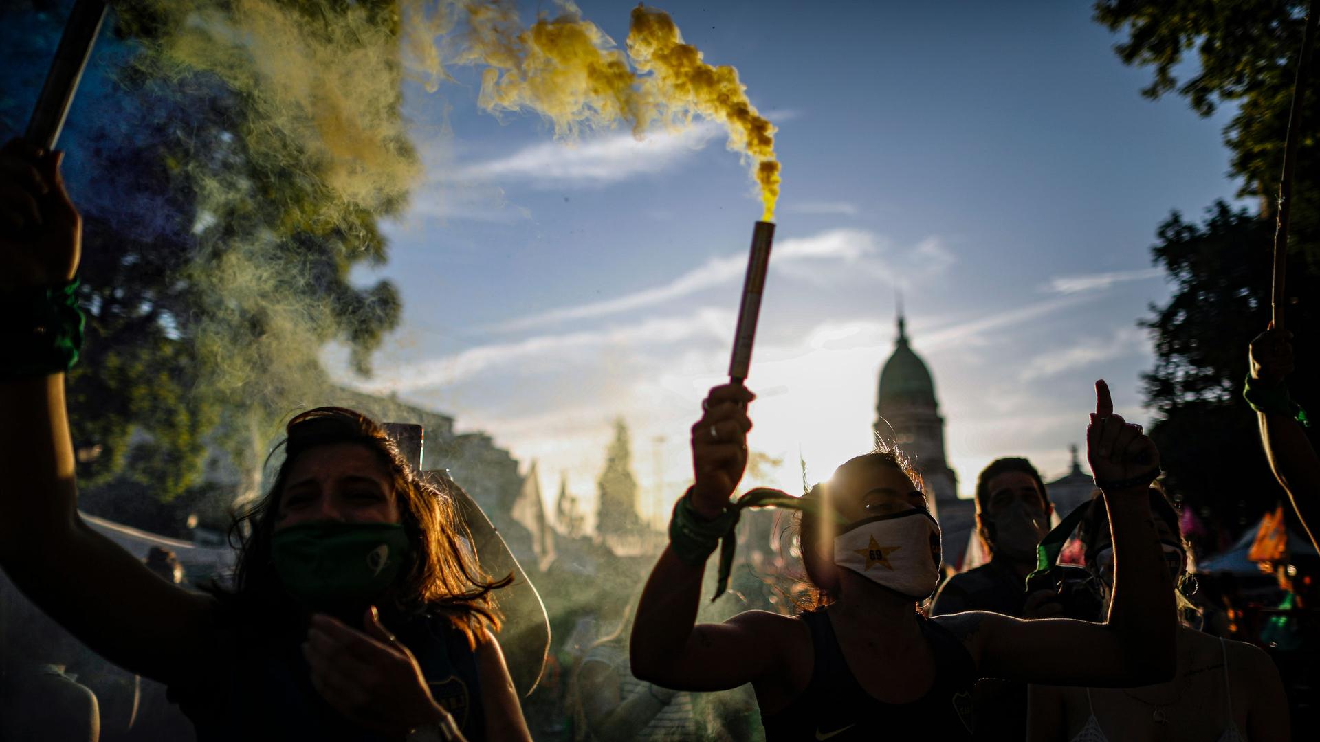 People are shown holding pipes letting off green smoke with the Argentine capital dome in the distance.