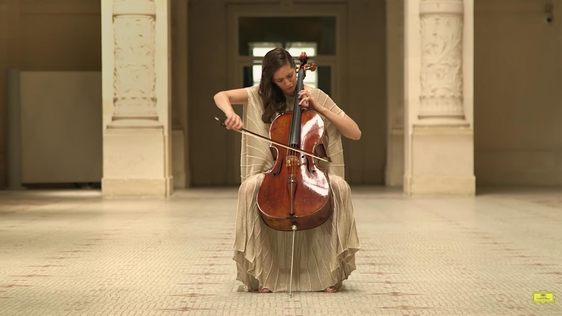 A woman playin cello appears in an empty museum hall.