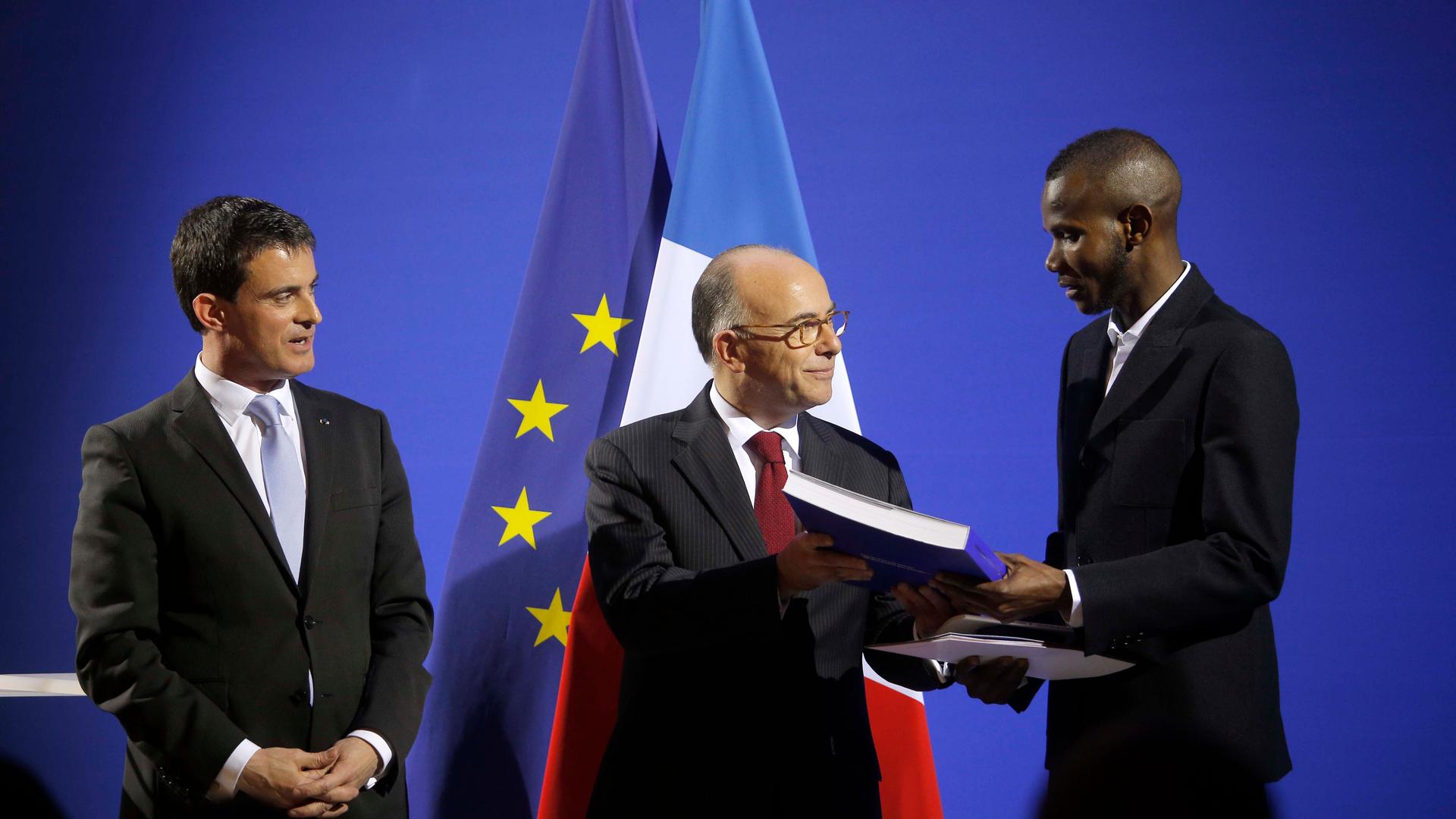French Prime Minister Manuel Valls, left, and French Interior Minister Bernard Cazeneuve, center, award citizenship to Lassana Bathily during a ceremony in Paris, Jan. 20, 2015.