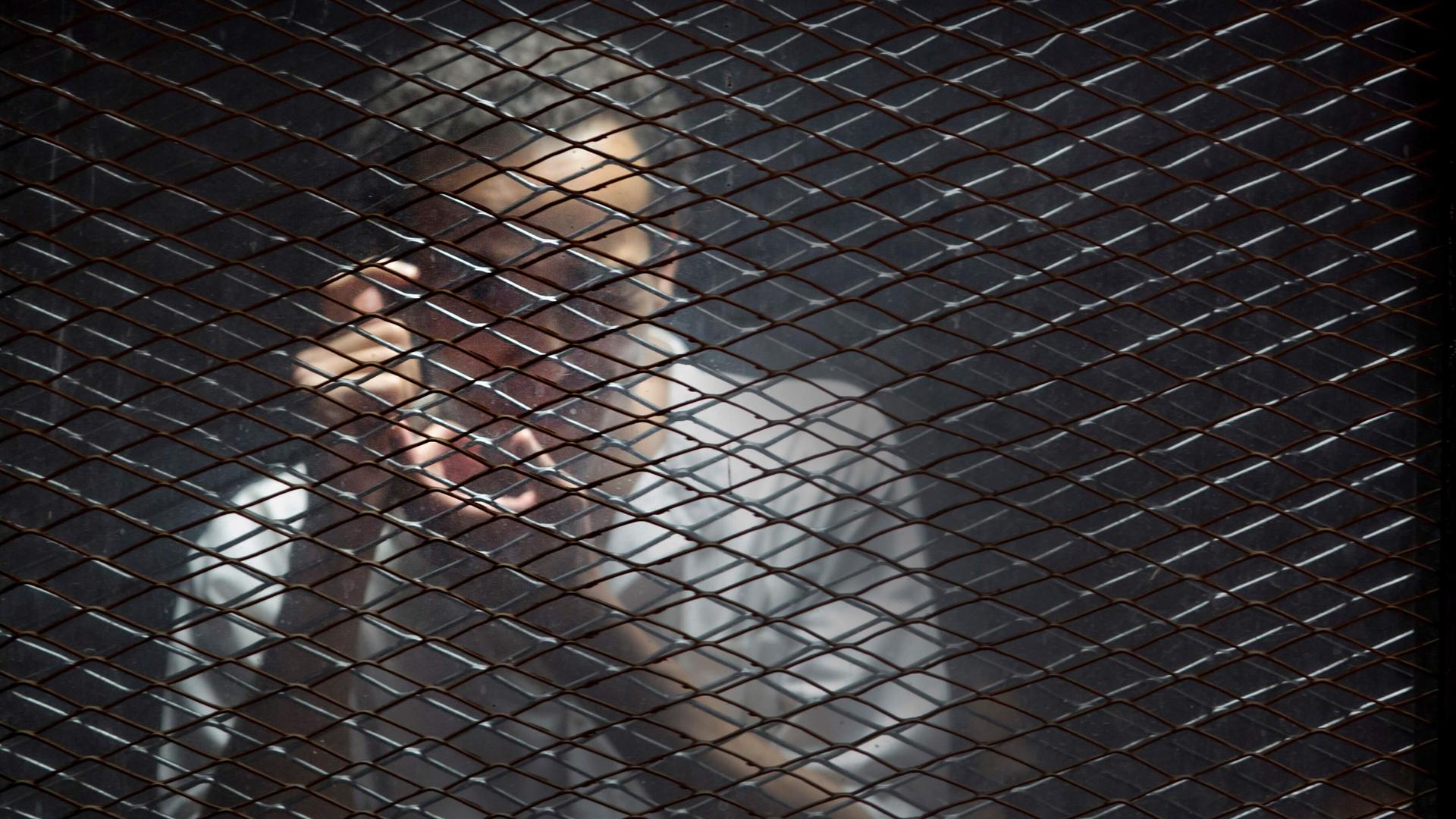 Egyptian photojournalist Mahmoud Abu Zied, known by his nickname Shawkan, gestures in a soundproof glass cage. 