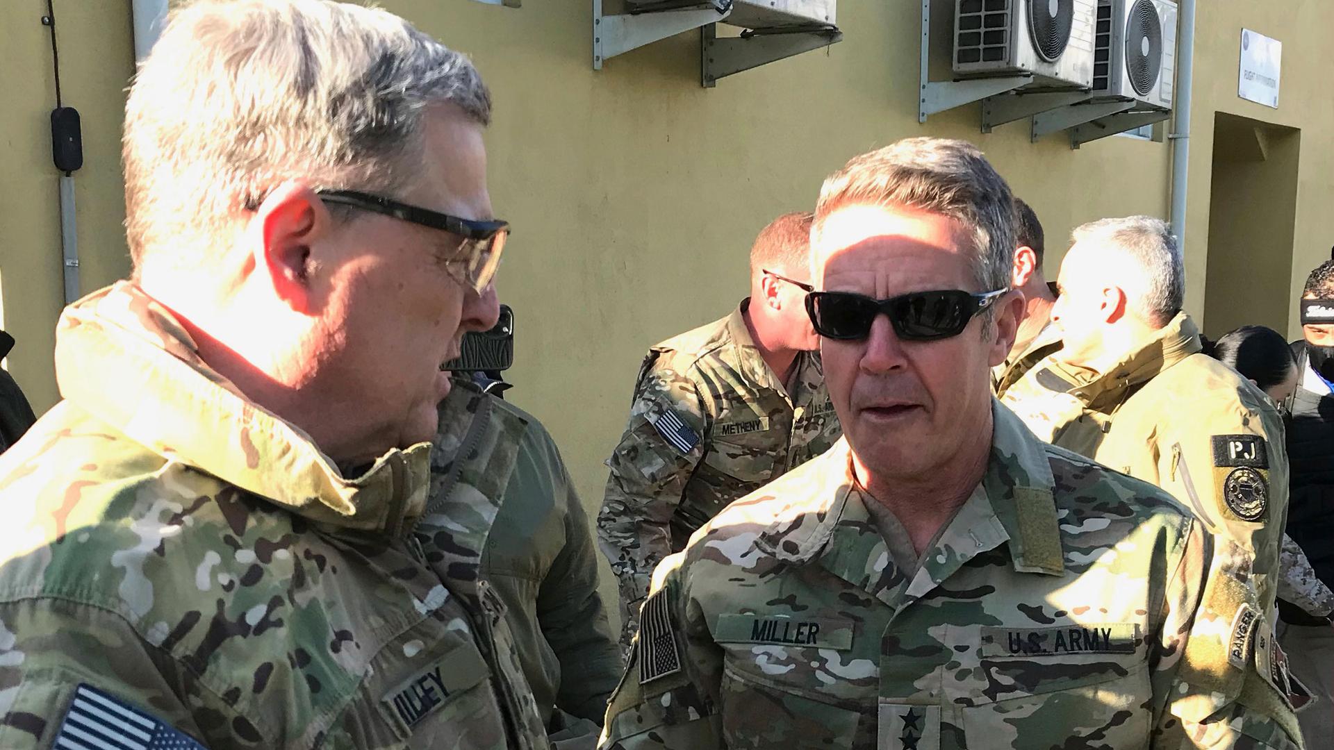 Gen. Mark Milley and Gen. Scott Miller are shown facing each other and wearing military fatigues.