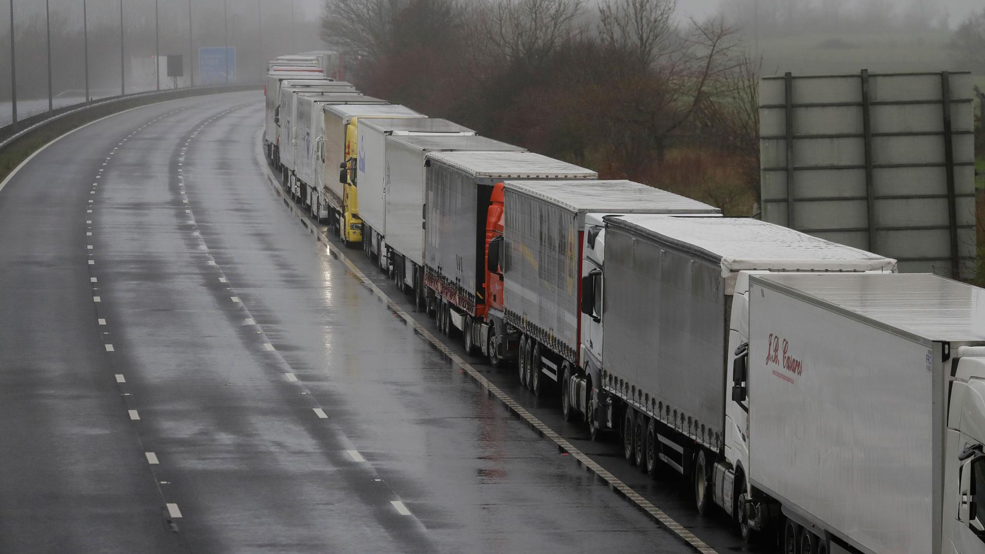 A long line of semi-trucks are shown bumper to bumper on a highway on an overcast day.