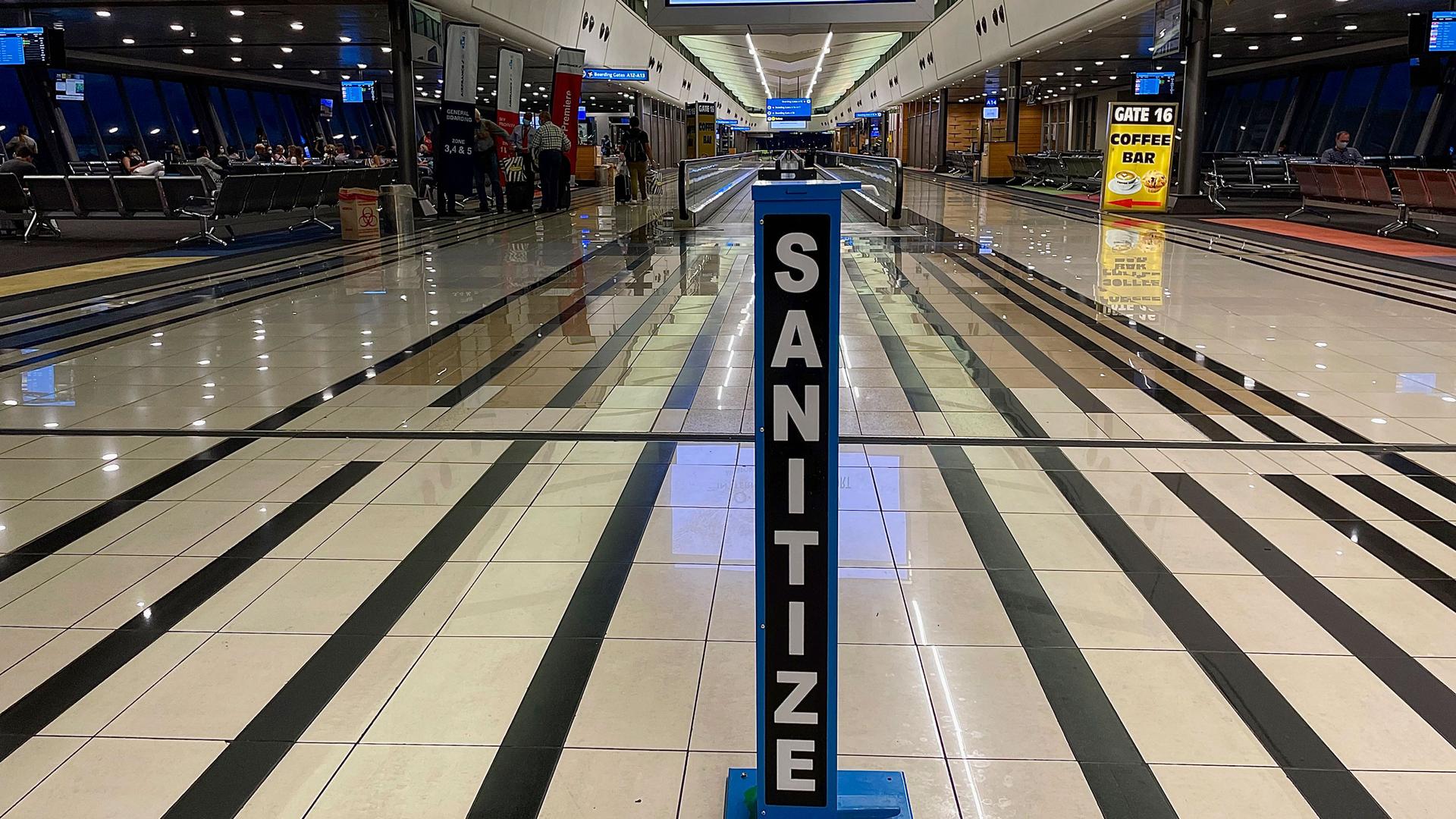 An airport terminal is shown nearly empty with black stripes along the flooring and a large hand sanitizing station in the center of the photogragh.
