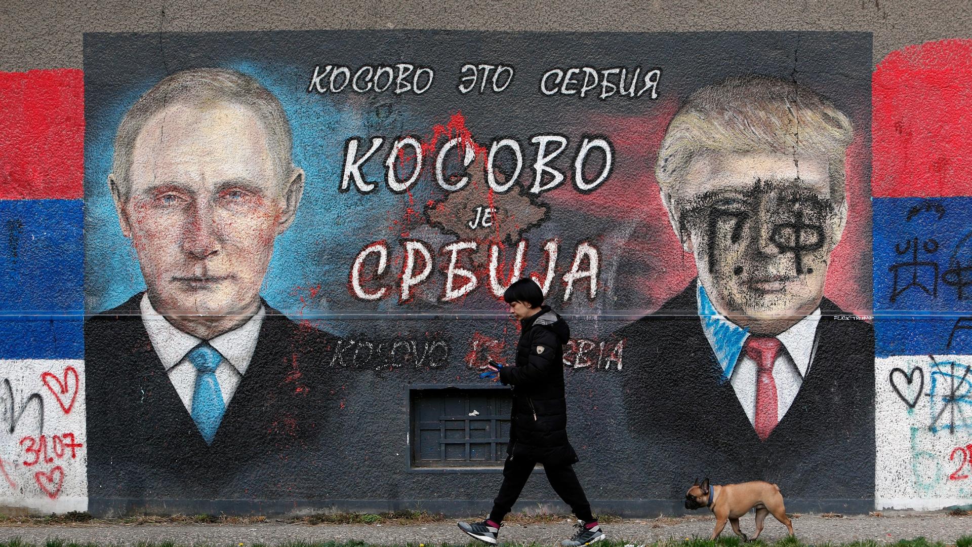 A woman with a dog passes by graffiti depicting the Russian President Vladimir Putin, left, and US President Donald Trump vandalized with paint in a suburb of Belgrade, Serbia, Nov. 3, 2020.