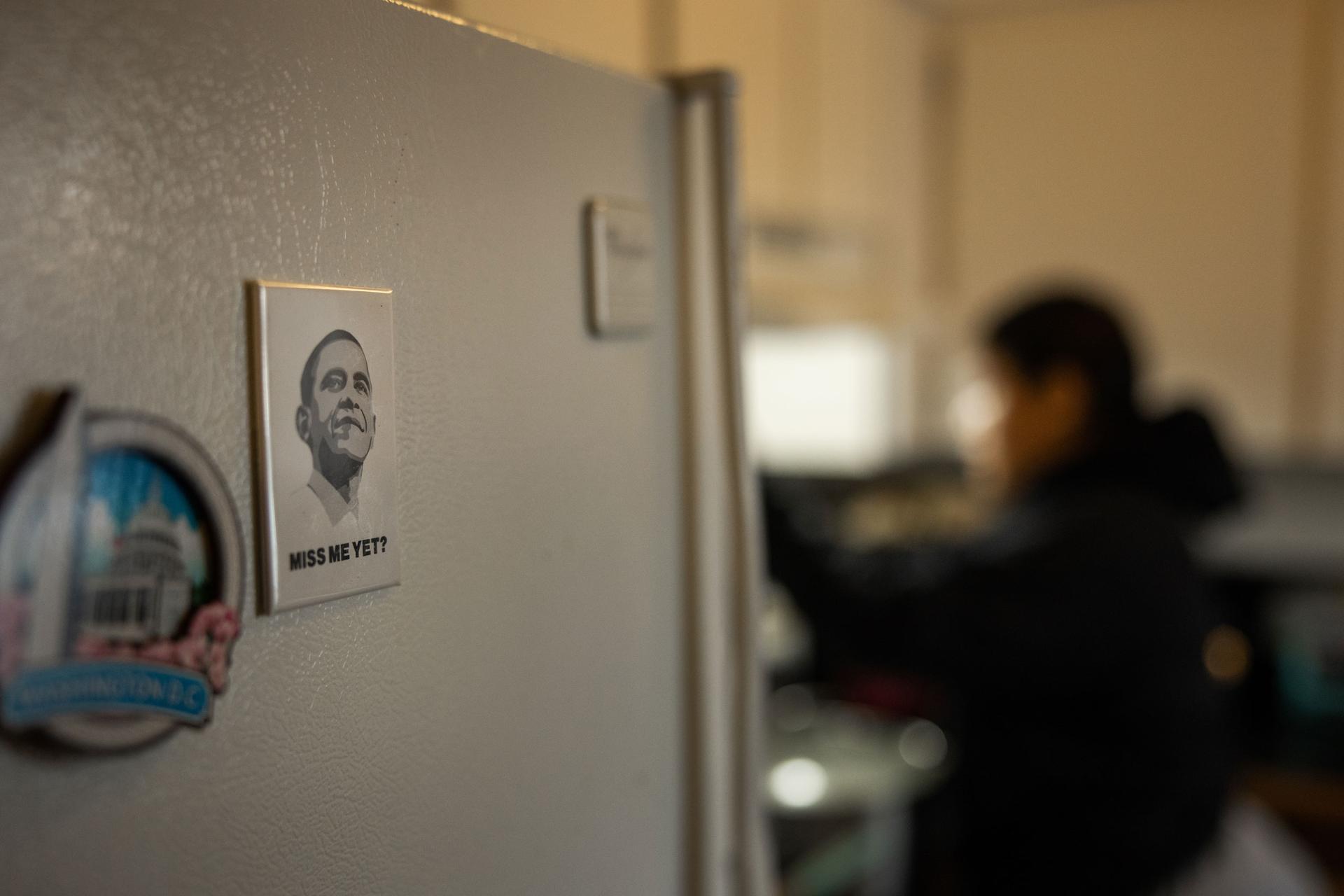 A magnet with a portrait of President Barack Obama is shown with a woman in the distance in soft focus.