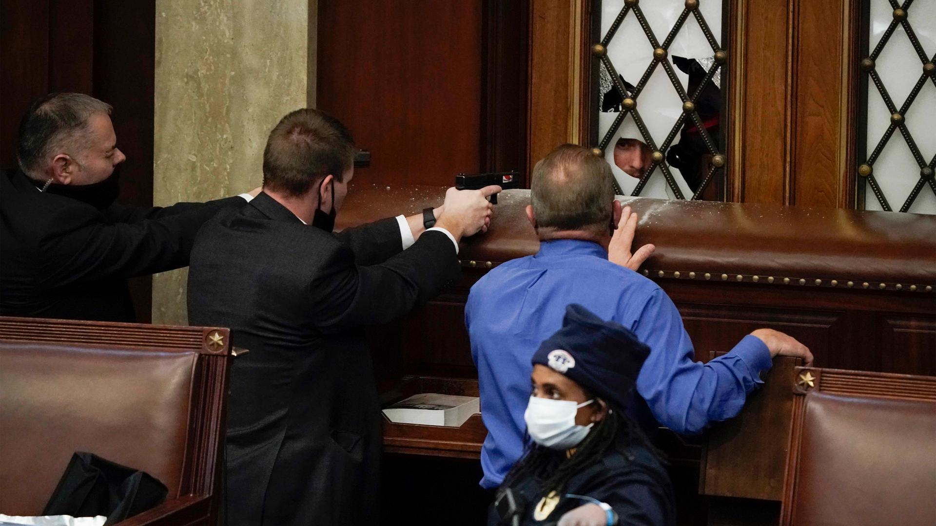 Police with guns drawn point at a rioter as a violent mob try to break into the House Chamber on Wednesday, Jan. 6, 2021, in Washington DC. 