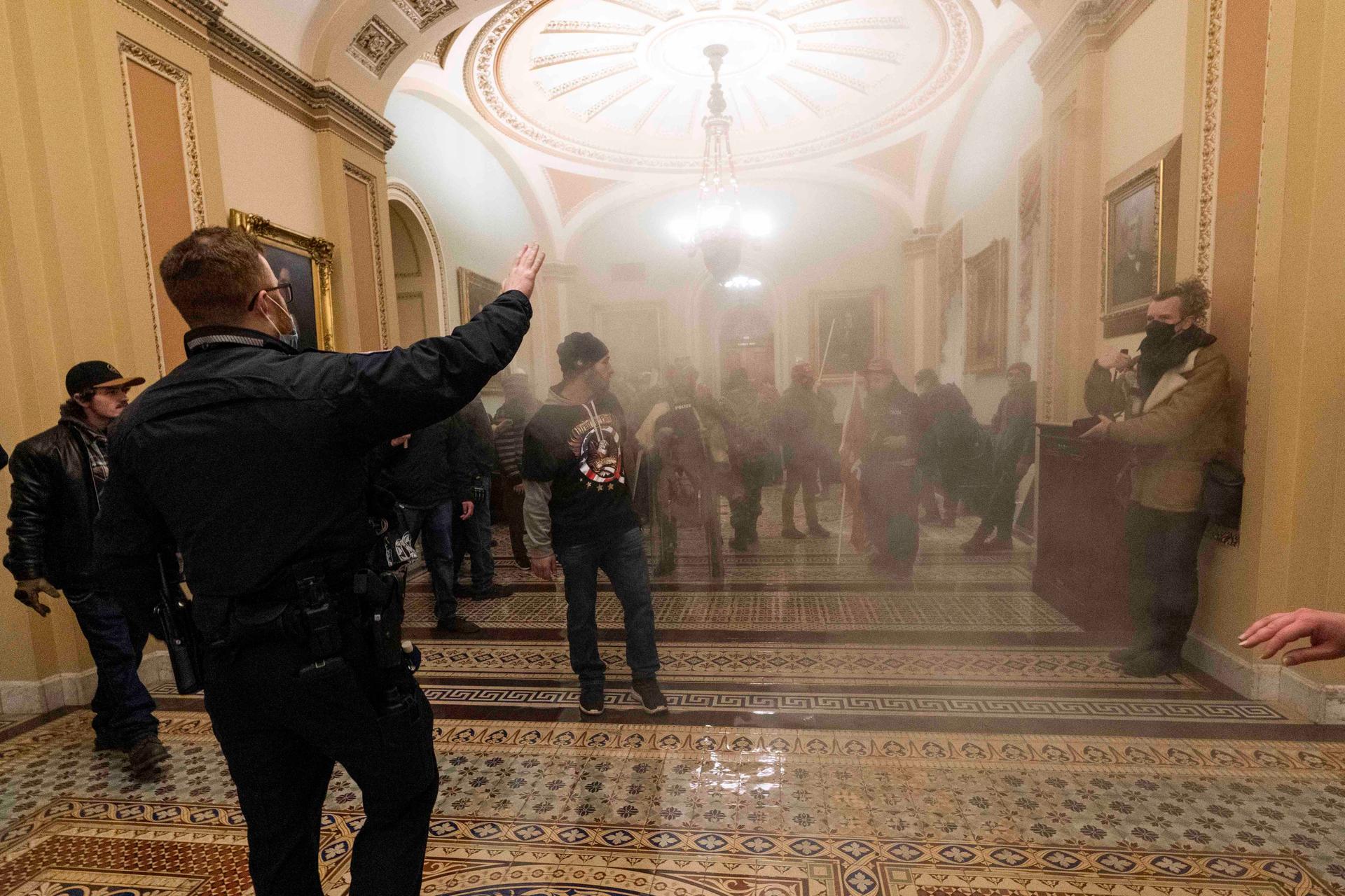 Smoke fills the walkway outside the Senate chamber as supporters of President Donald Trump are confronted by US Capitol Police officers inside the Capitol, Wednesday, Jan. 6, 2021, in Washington, DC. 