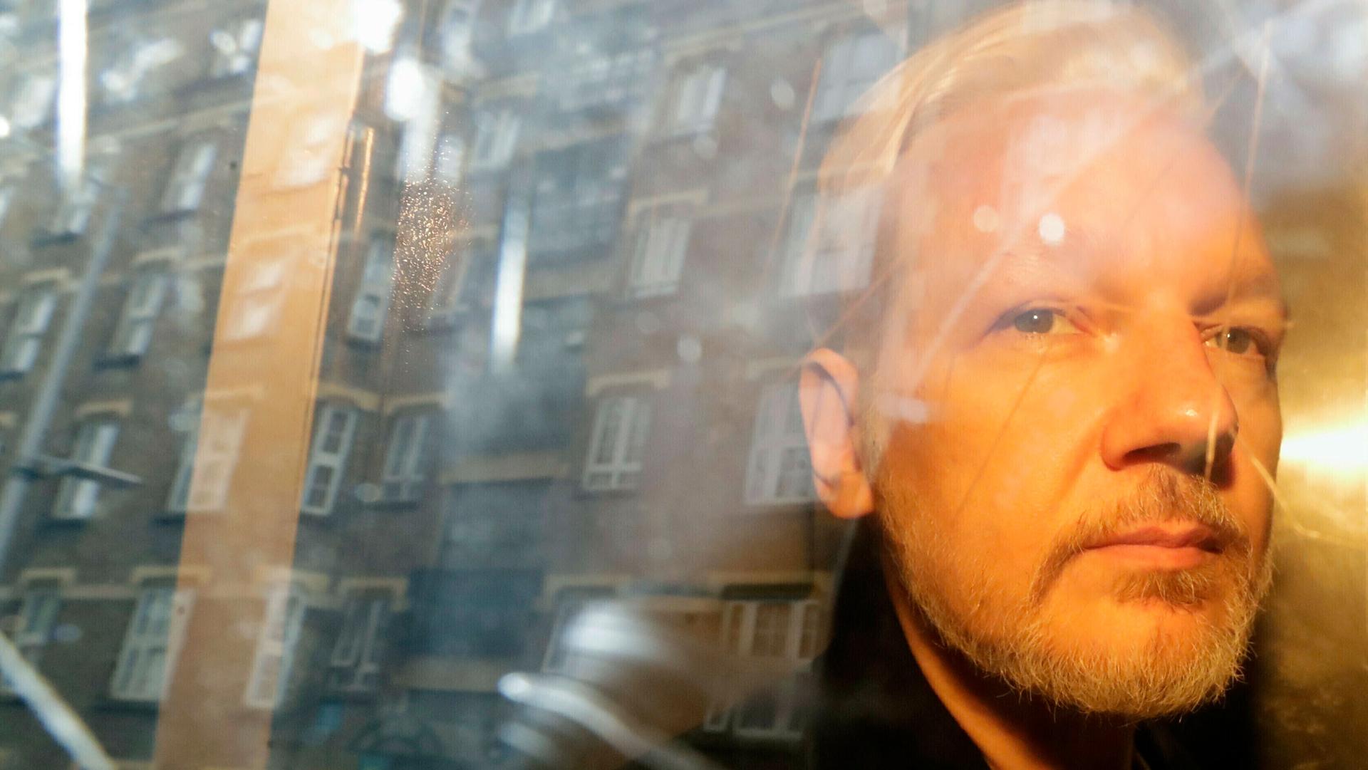 WikiLeaks founder Julian Assange is shown through the glass of a car door with the reflection of buildings in the distance.