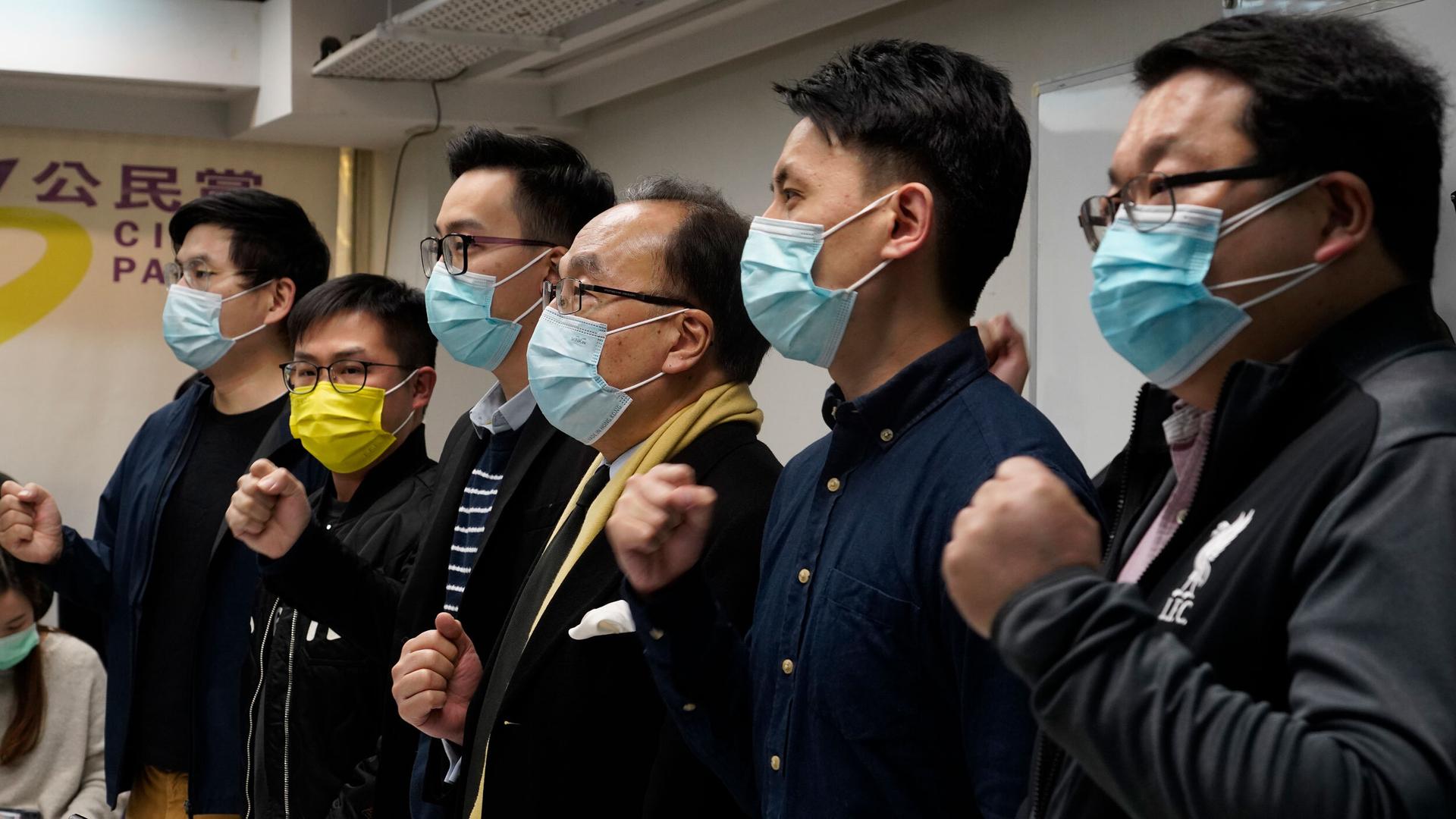 Six people wearing medical masks stand and shout slogans. 