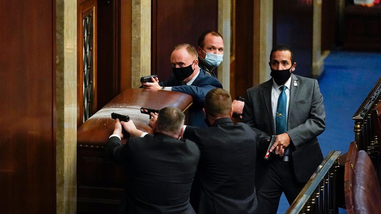 US Capitol police with guns drawn stand near a barricaded door as members of a mob try to break into the House Chamber in Washington.