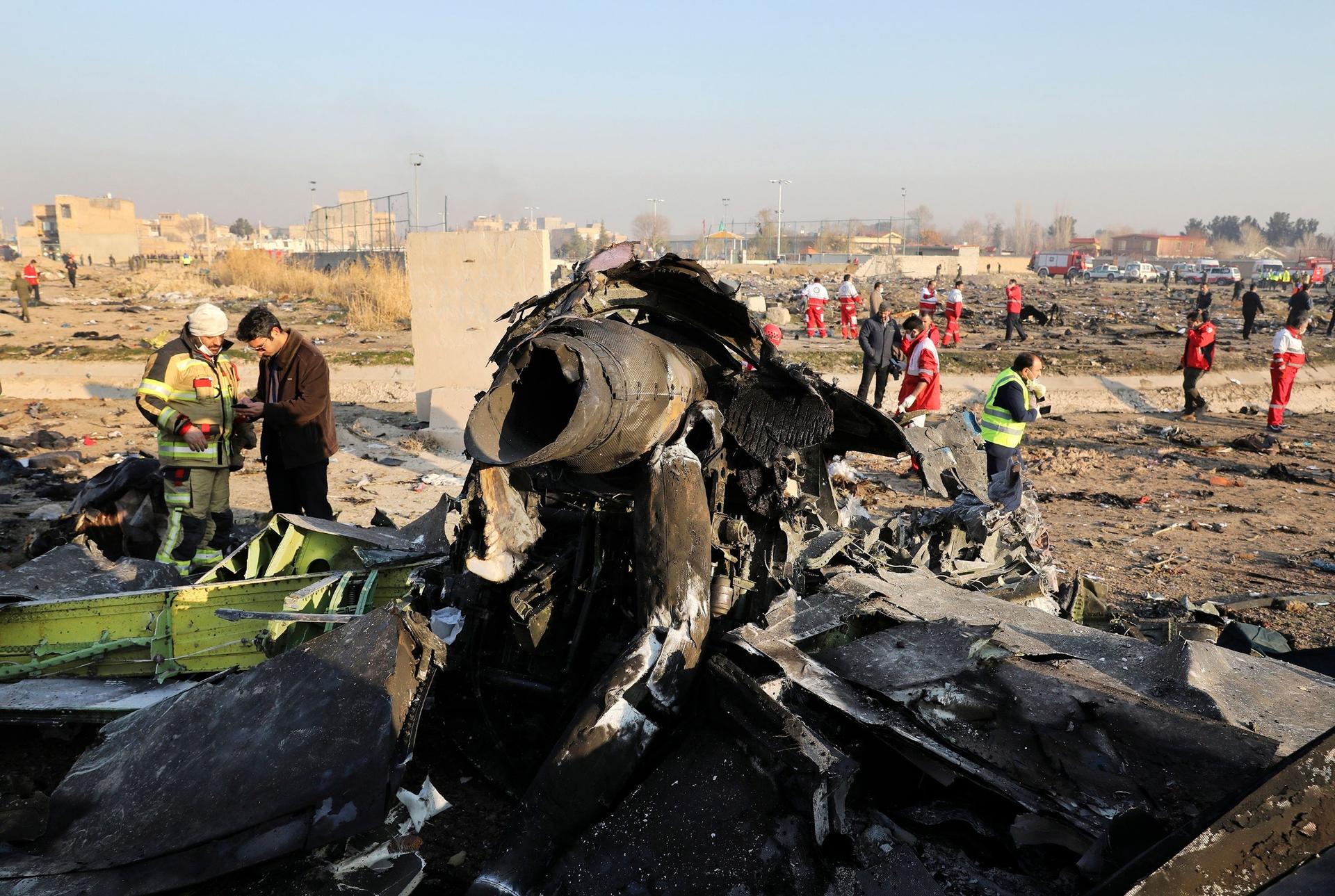 The charred remains of a passenger aircraft is shown with several inspectors shown on the scene in the distance.