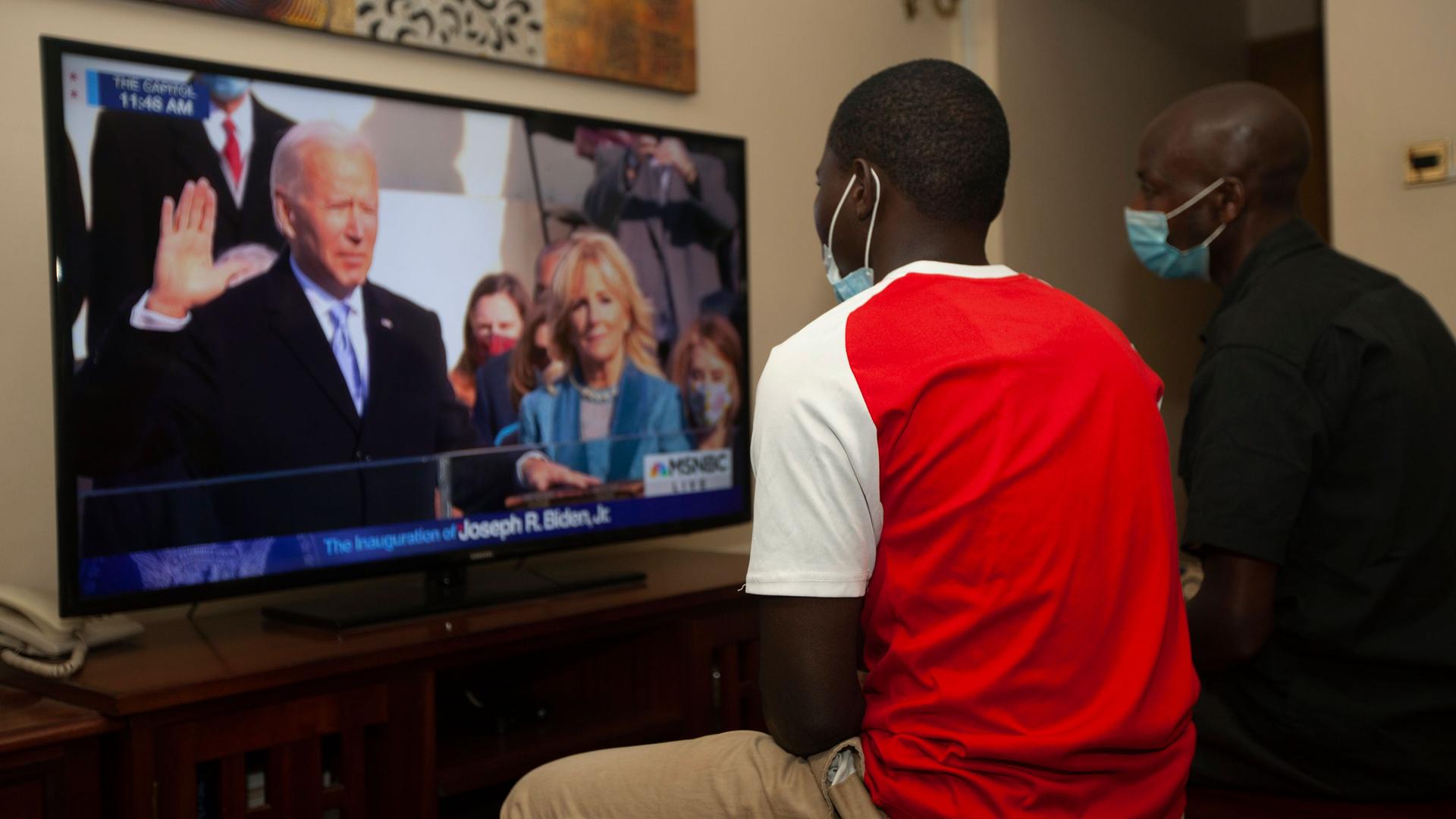 Two Kenyan men are shown sitting and watching President-elect Joe Biden's inauguration on TV. 