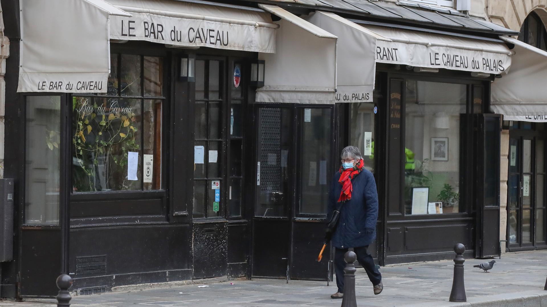 A person walks past a closed restaurant in Paris wearing a face mask. 