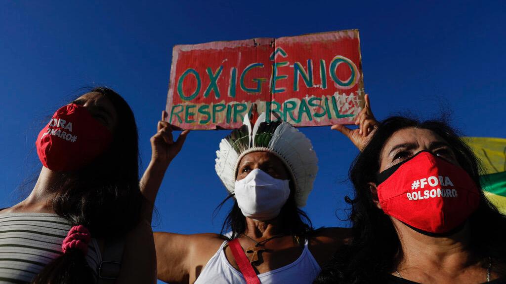 Demonstrators wearing masks with text written in Portuguese that read "Bolsonaro out," and a sign with the phrase "Oxygen, Breathe Brazil," protest against the government's response in combating COVID-19 and demanding the impeachment of Brazil's President