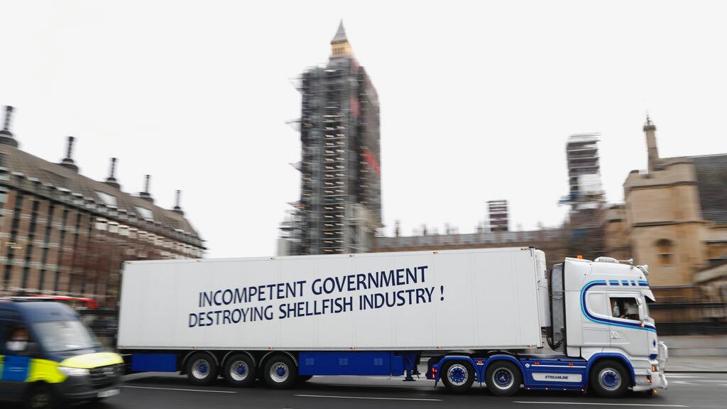 A shellfish export truck with a protest sign written across the trailer "Incompetent Government Destroying Shellfish Industry" drives past the Palace of Westminster in London 