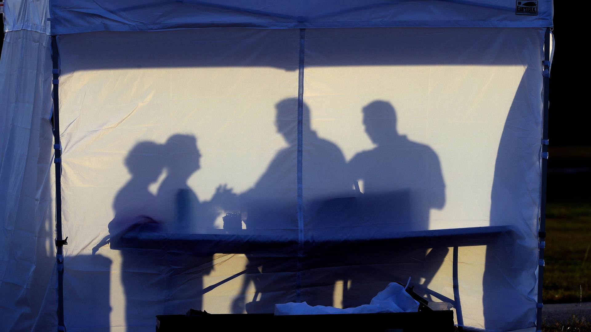The silhouette of four people are show against the white panel of a tent.
