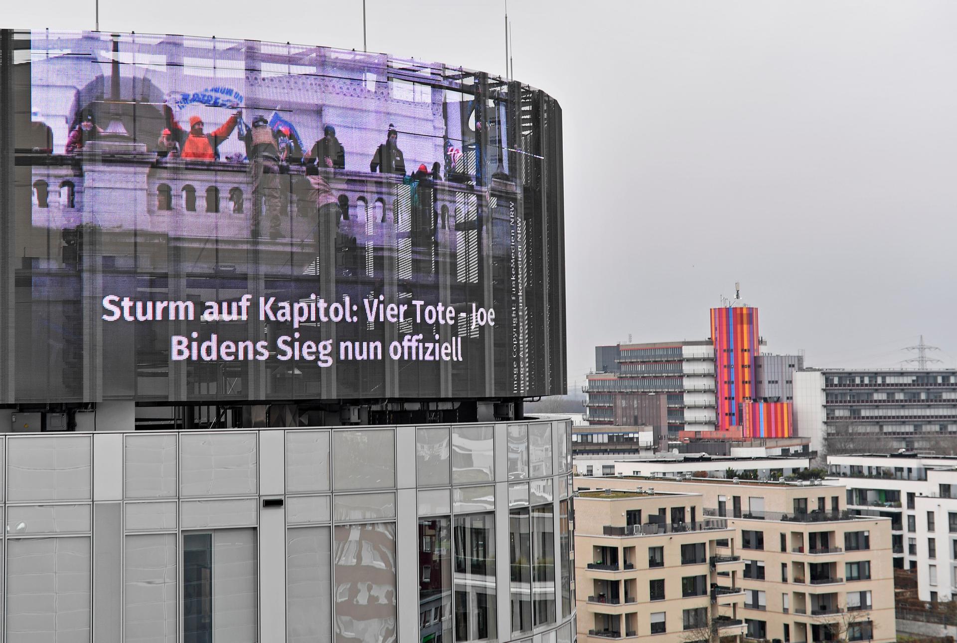 A big news screen on a building in Essen, Germany, showing protesters on the US Capitol in Washington, a headline reads 