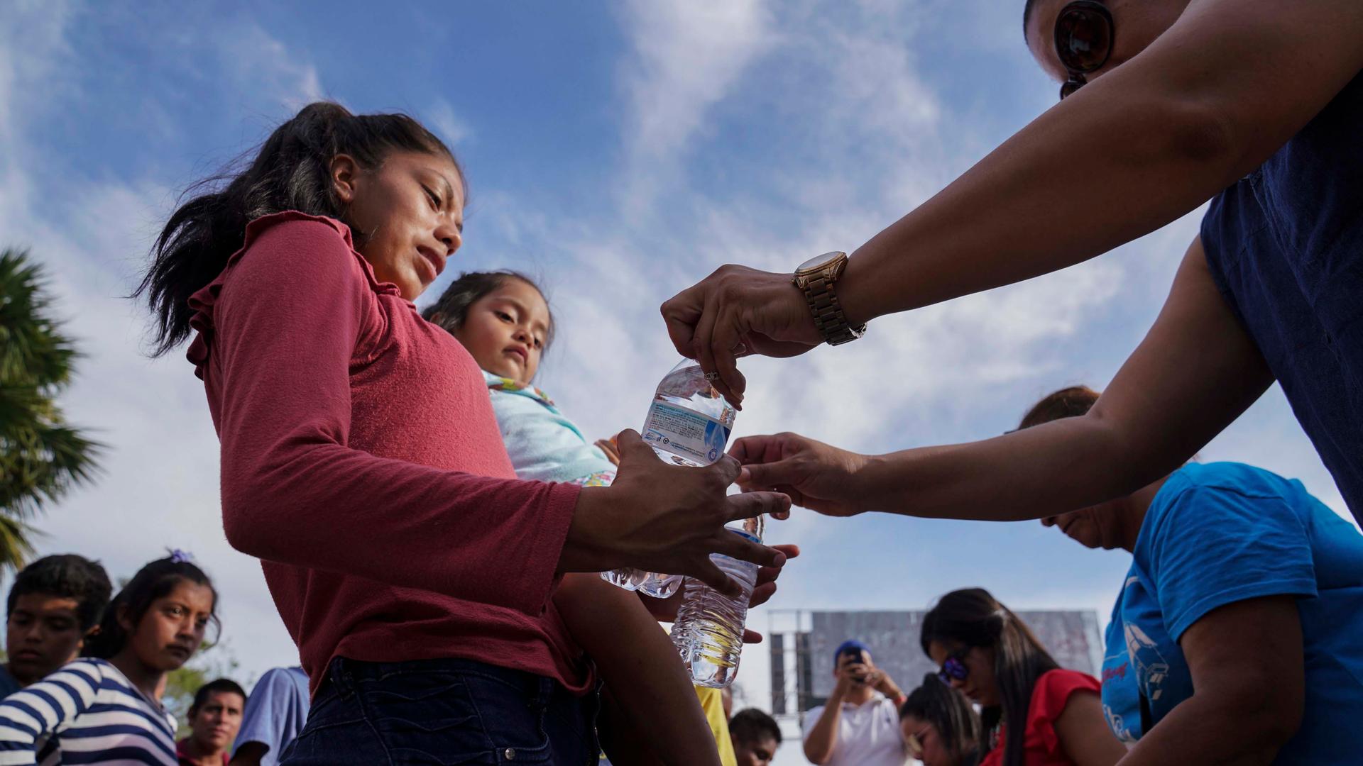 n this Aug. 30, 2019, photo, migrants, most who were returned to Mexico under the Trump administration’s “Remain in Mexico” program, receive bottles of water given by volunteers in an encampment near the Gateway International Bridge in Matamoros, Mexico. 