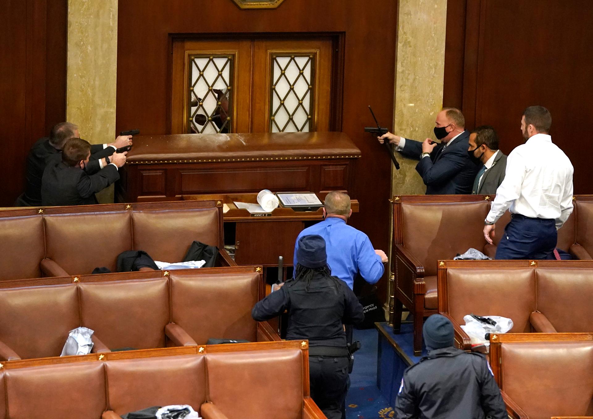 US Capitol police officers point their guns at a door that was vandalized in the House Chamber during a joint session of Congress on Jan. 06, 2021, in Washington, DC.