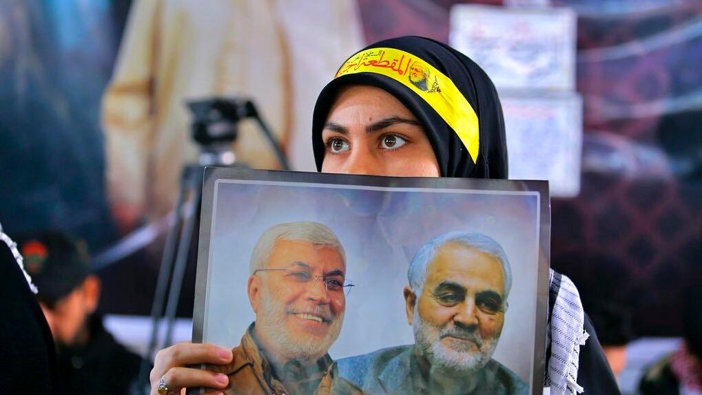 A woman holds a poster showing Gen. Qasem Soleimani, right, head of Iran's Quds force and Abu Mahdi al-Muhandis, deputy commander of the Popular Mobilization Forces, during the procession to commemorate the first anniversary of their killing by a US drone