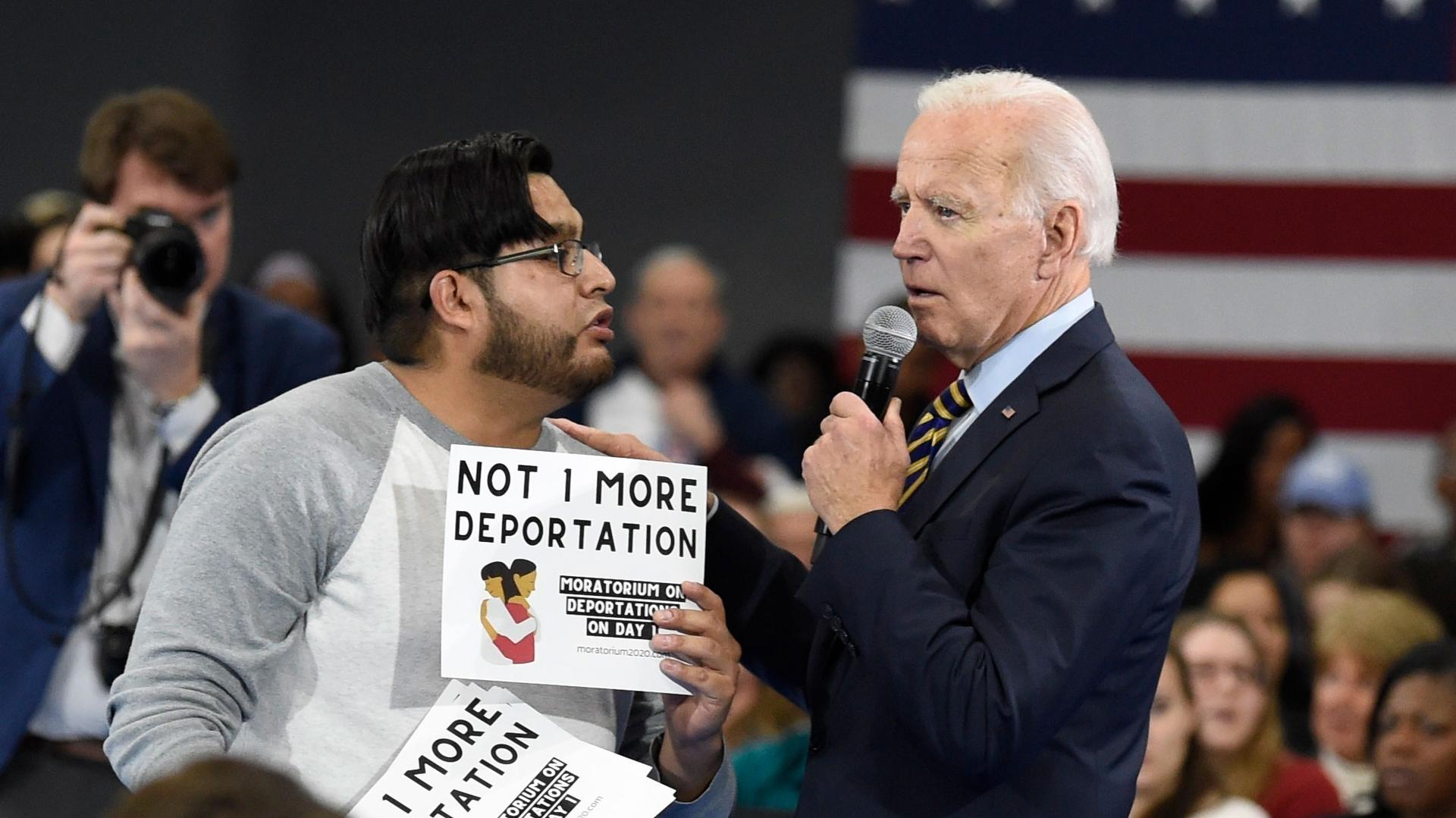 A man is shown holding a sign that reads "Not 1 more deportation" while speaking to Joe Biden who is holding a microphone.