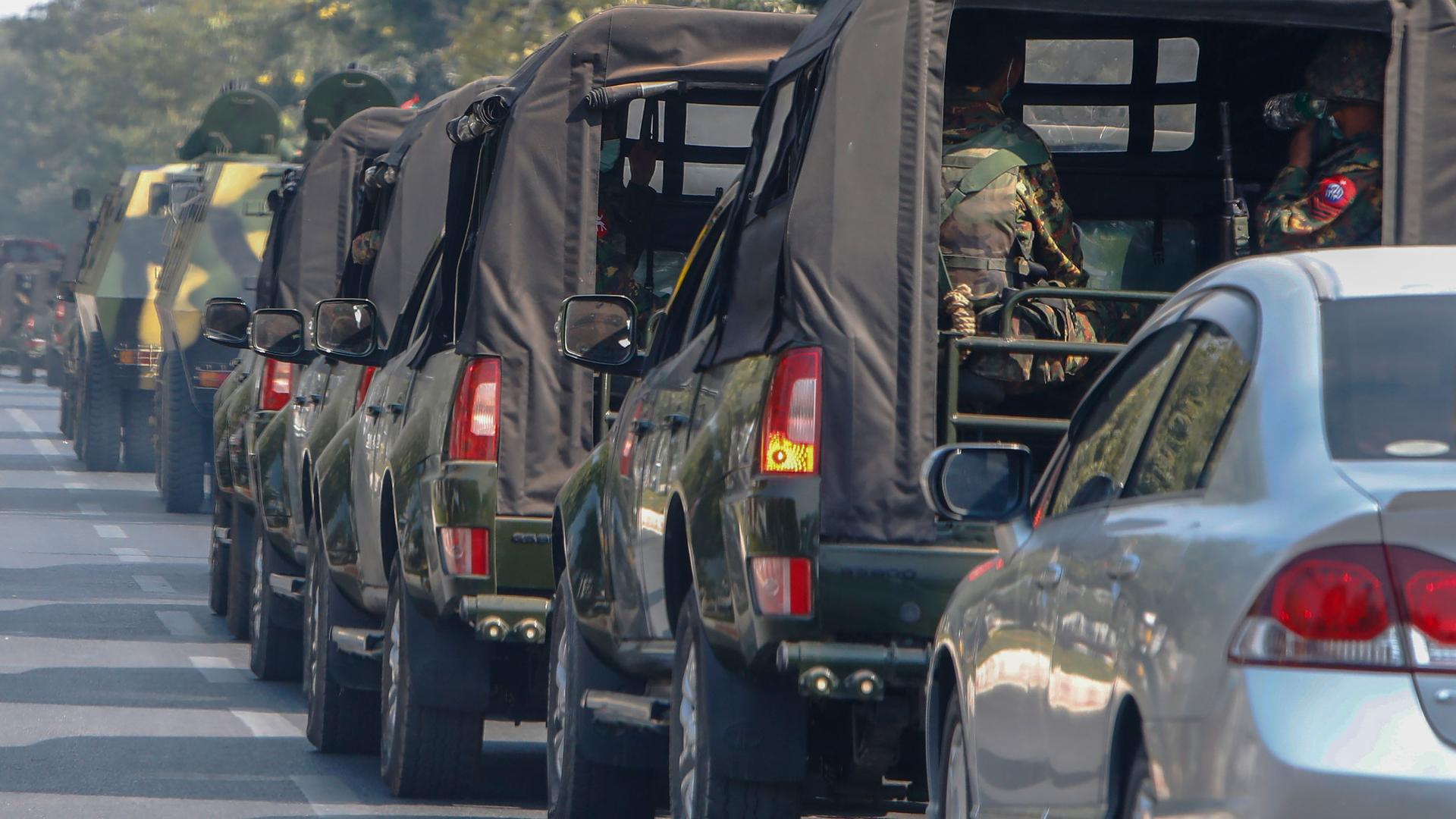 A long ling of military vehicles are shown painted in green-colored camoflage driving on a road.