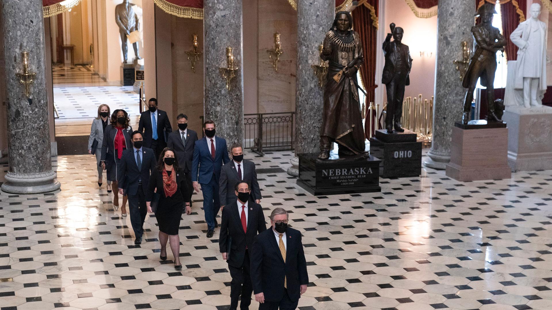 Two liines of lawmakers are shown walking across a black and white checkered floor in a large room with tall marble pillars.