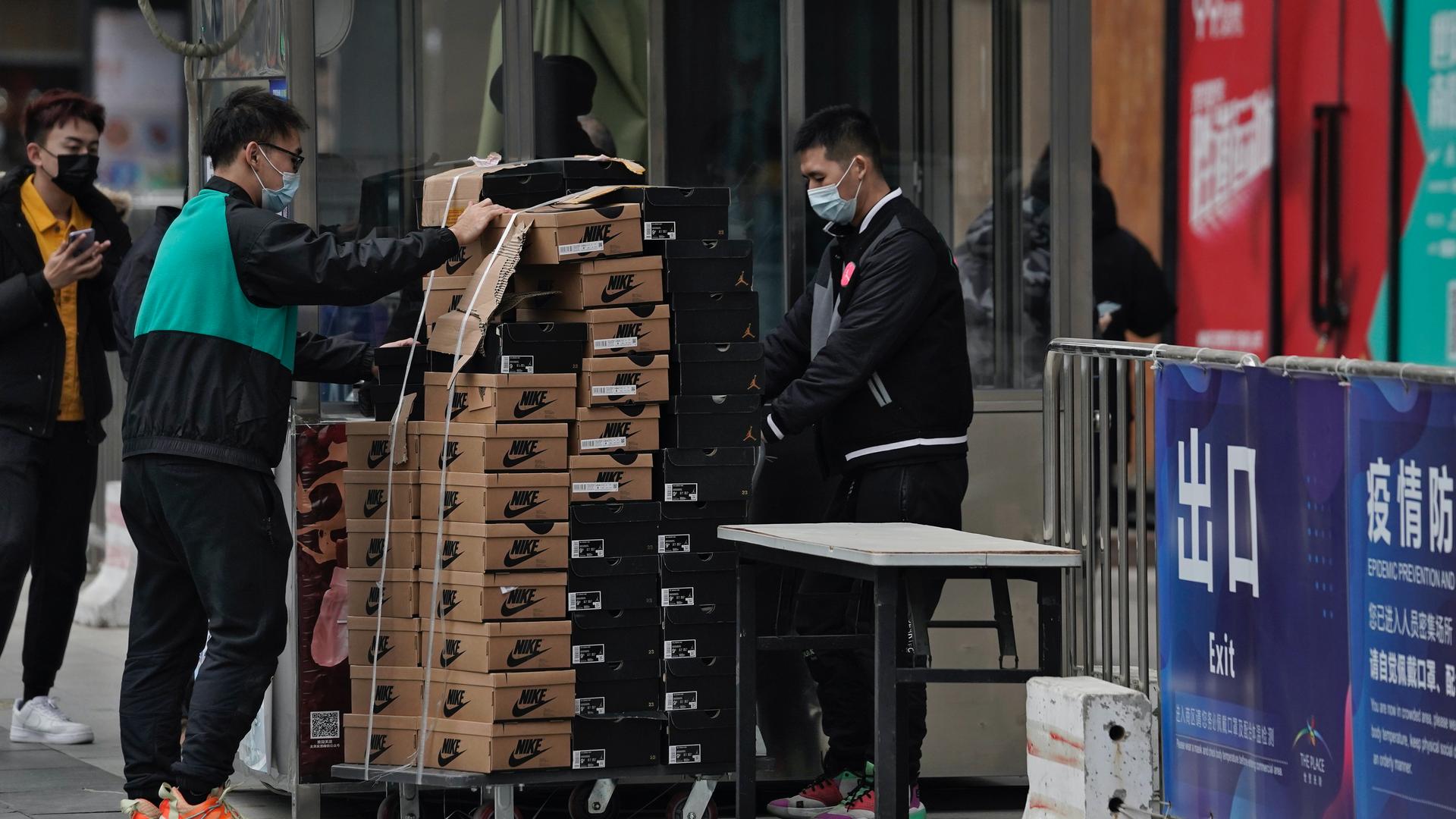 Workers wearing face masks to help curb the spread of the coronavirus push a cart loaded with shoes made by Nike past a security post at a shopping mall in Beijing, Jan. 14, 2021. China's exports rose in 2020 despite pressure from the coronavirus pandemic