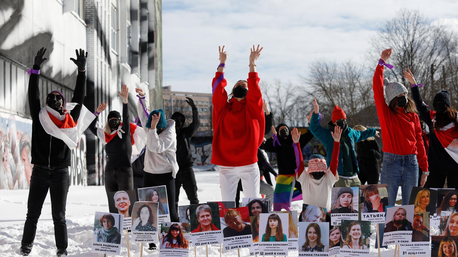 A group of women, several wearing red, are shown with their hands in the air and with dozens of photographs in front of them.