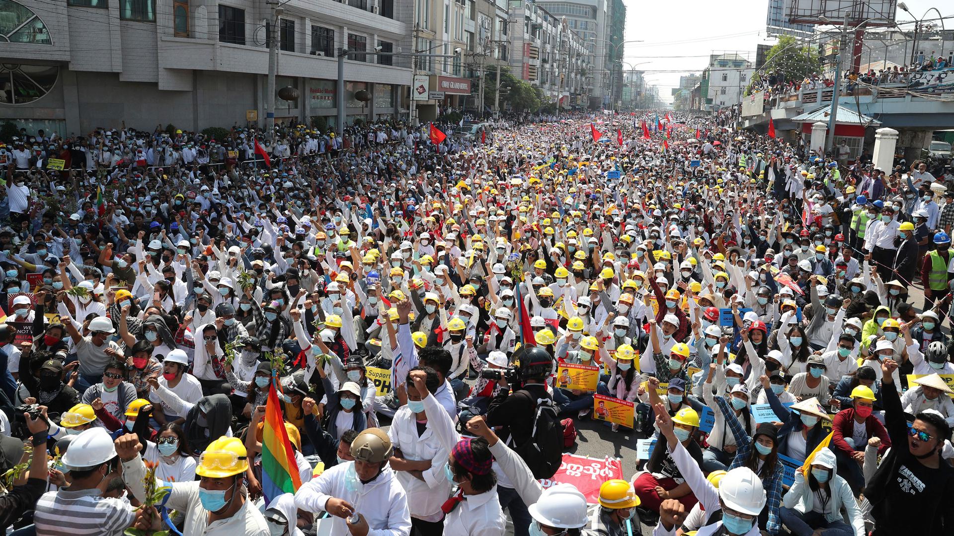 Thousands of people are shown marching in a street with many wearing yellow construction helmets.