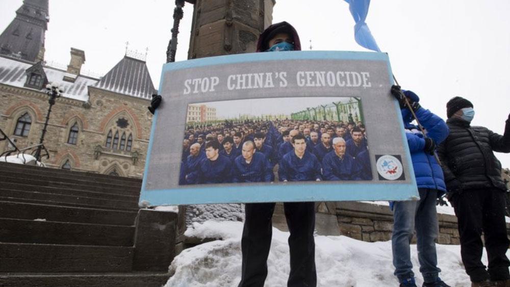 A protester is shown holding a large sign the has the words, "Stop China's Genocide" on it.