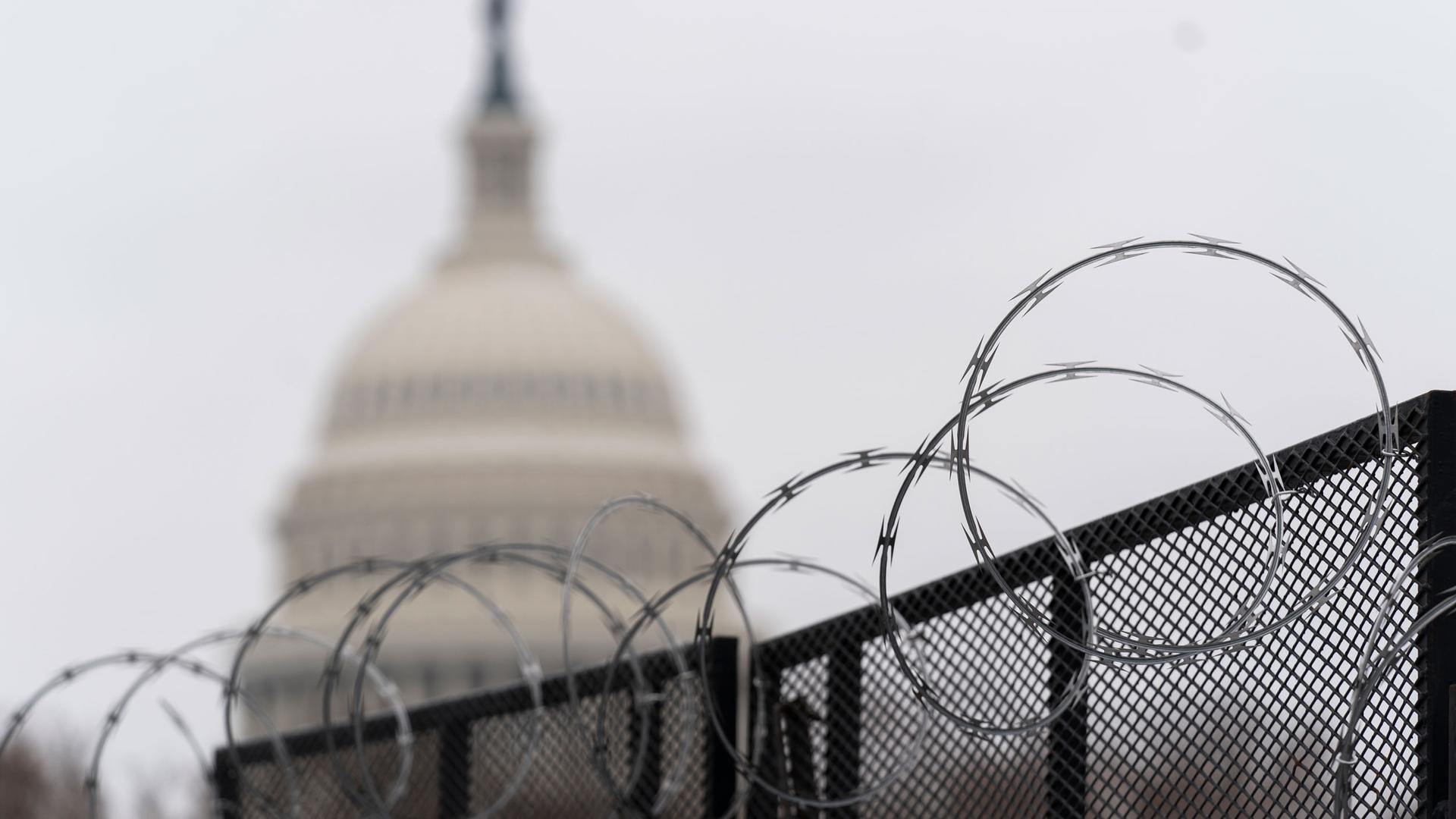 Circular razorwire is shown at the top of a fence with the dome of the US Capitol building in the distance and in soft focus.