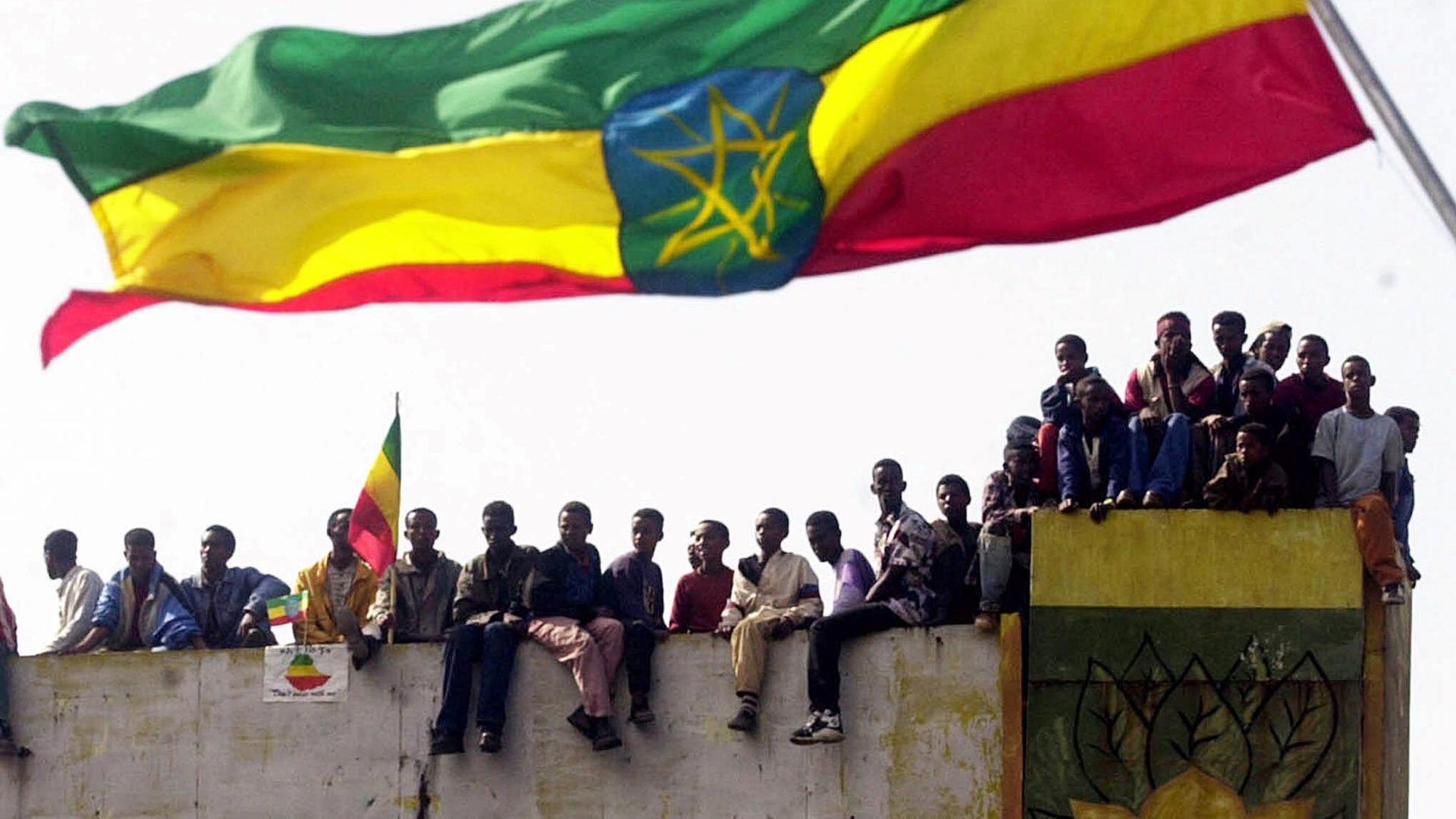A huge flag of Ethiopia waves with people sitting underneath it