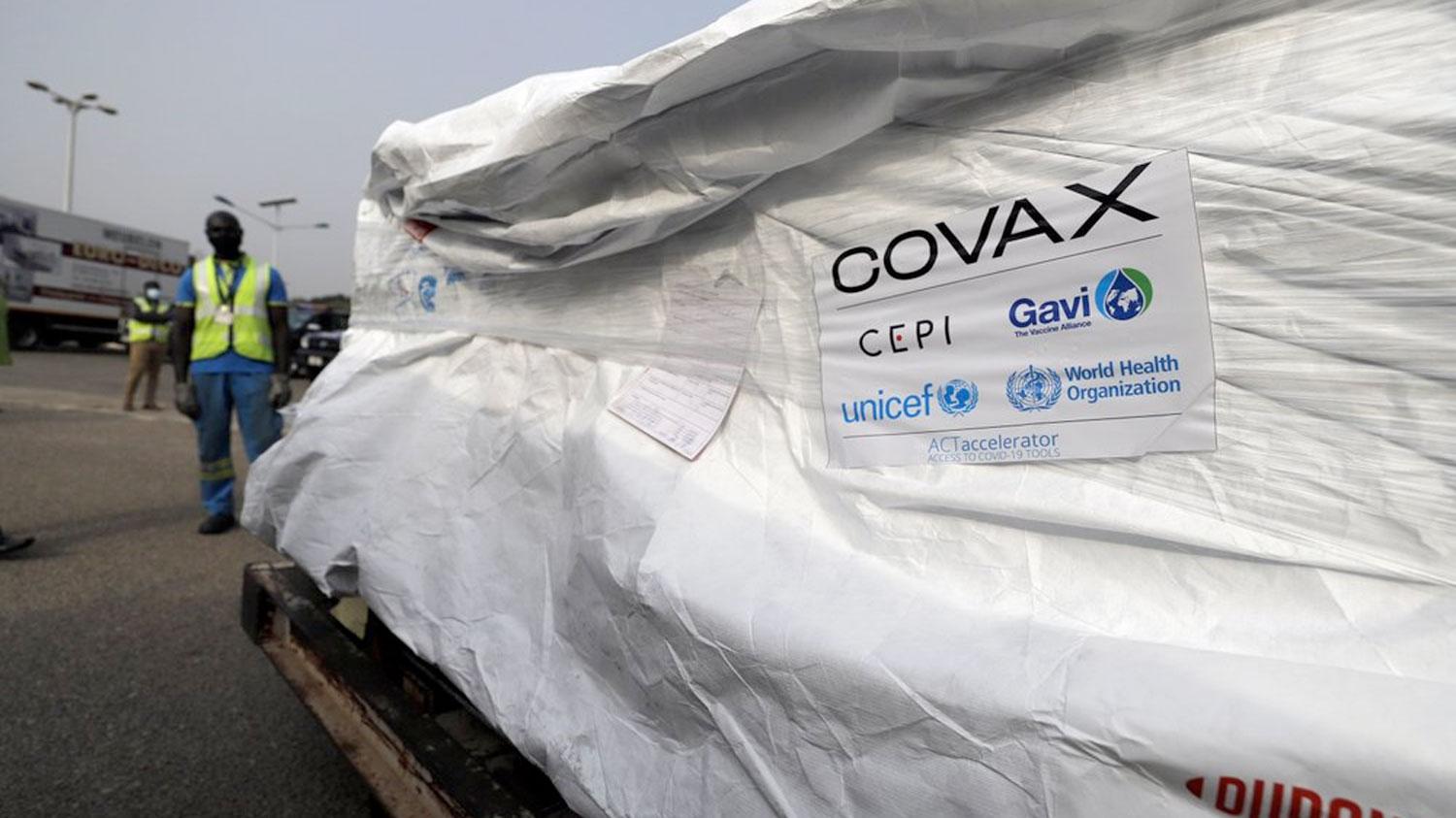 A large pallet is shown covered in a white wrapping with the logo for COVAX posted on the side.