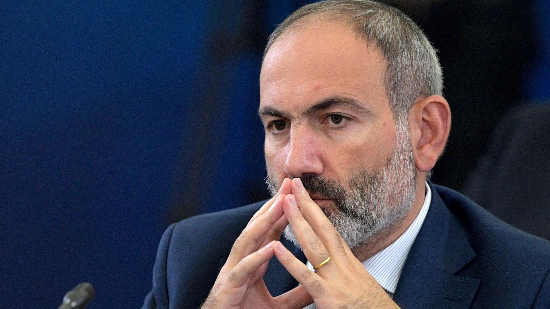 Armenian Prime Minister Nikol Pashinyan is shown with the fingertips of his hands pressed against each other and next to his mouth.