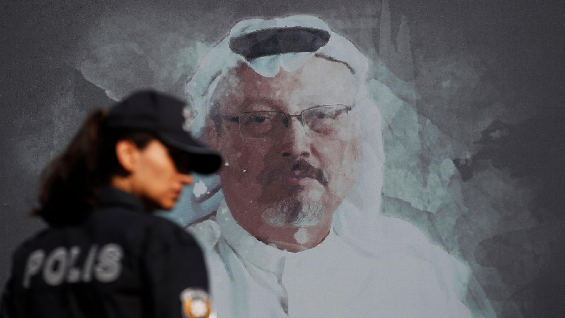 A police officer is shown looking over her right shoulder and wearing a hat with a portrait of slain Saudi journalist Jamal Khashoggi on the wall behind her.