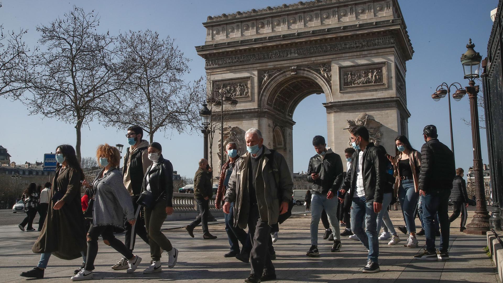 A crowd of people are shown walking with Paris' iconic Arc de Triomphe in the background.