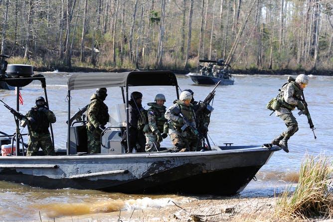 Navy soldiers in training unload a boat during a field training exercise.