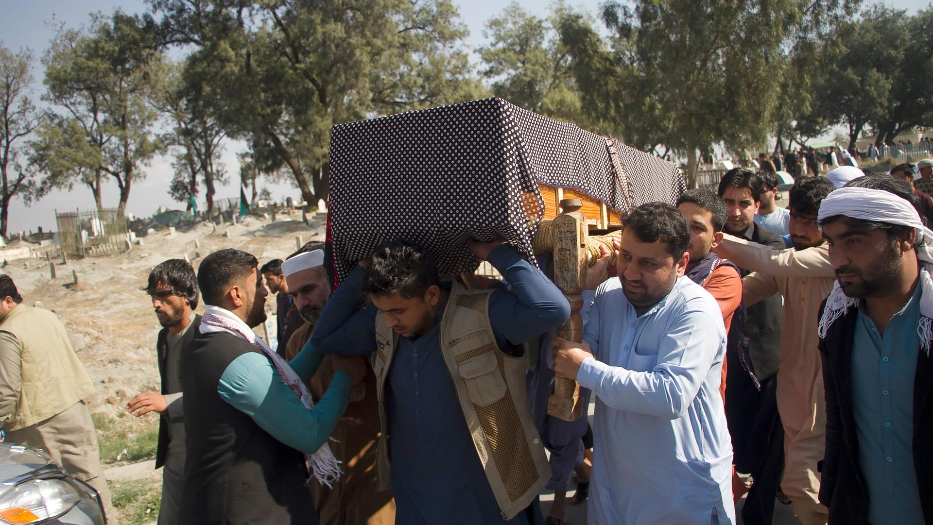 A group of men are shown carrying a casket on their shoulders drapped with a blanket.