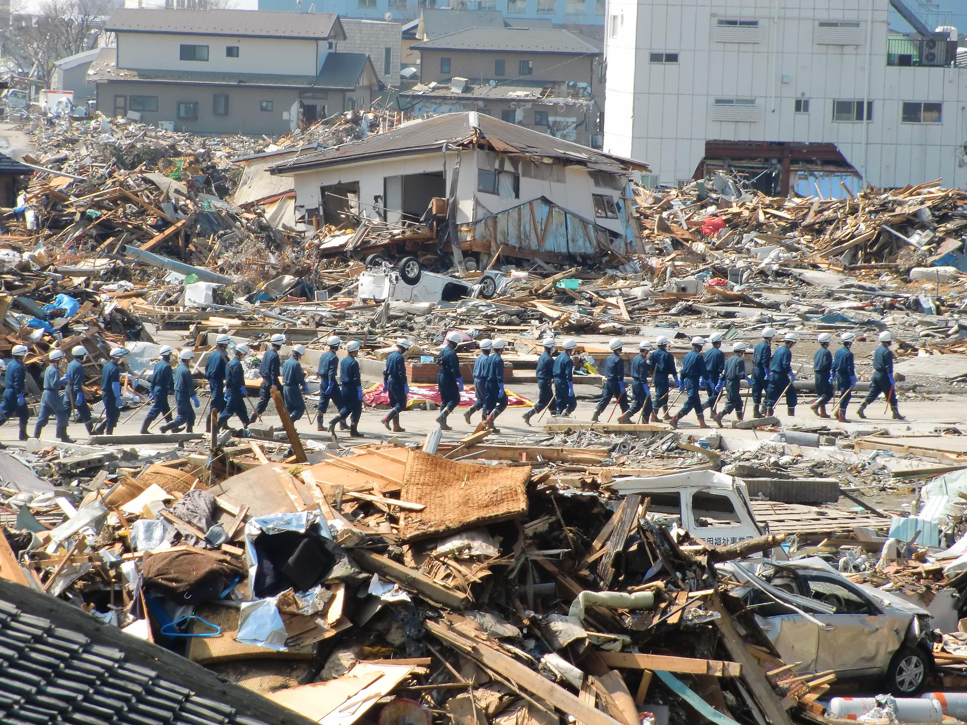 A long line of Japan's Self Defense Forces are shown wearing blue protective outfits and walking among the rubble of Ishinomaki.