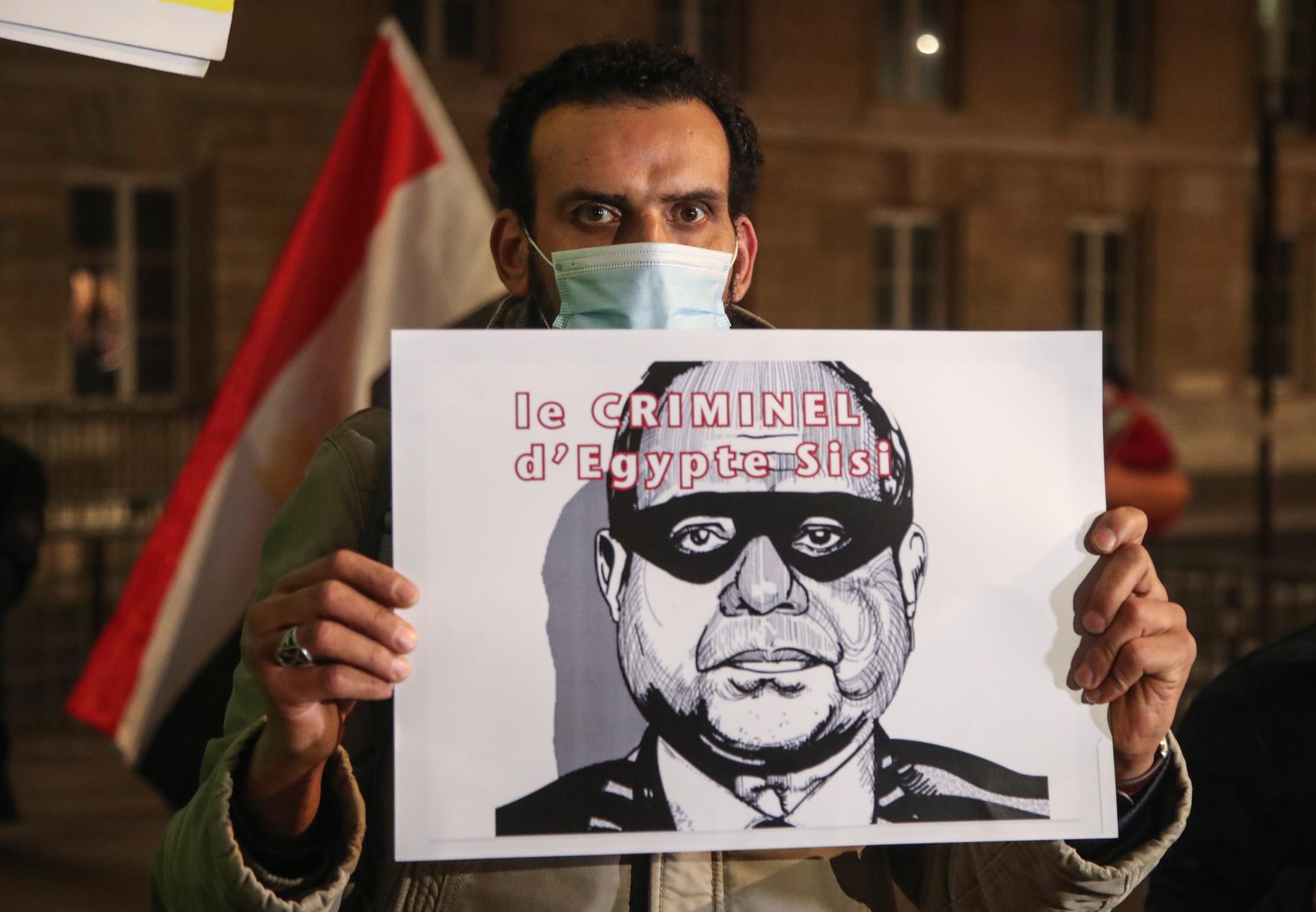 A man holds a placard depicting Egyptian President Abdul Fattah al-Sissi and reads he is a criminal as he stages a protest by the National Assembly in Paris, Dec. 8, 2020. 